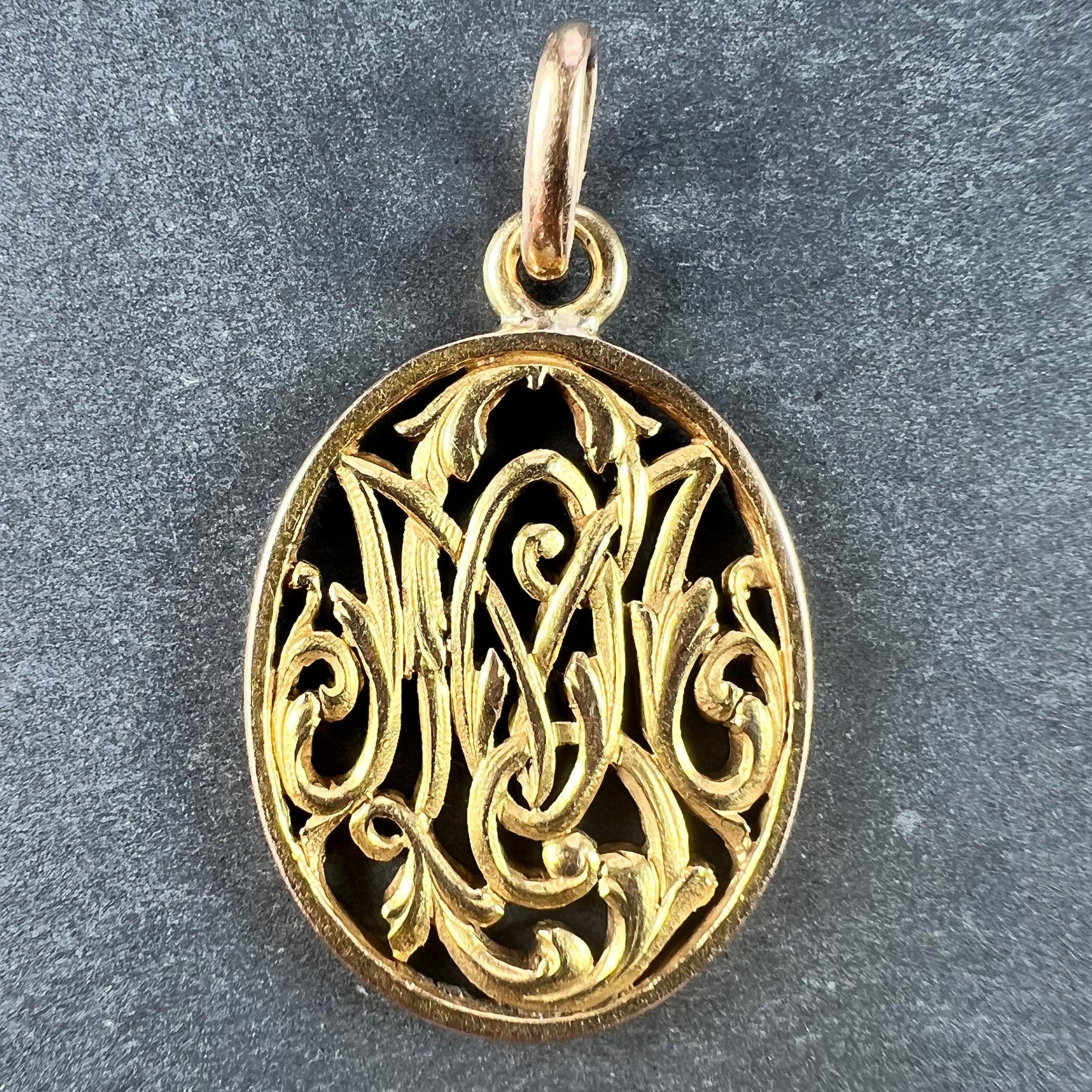 An antique French 18 karat (18K) yellow gold charm pendant designed as an oval pierced medal detailing the monogram OM or MO with the initials M and O intertwined and surrounded by curls and scrolls of engraved filigree work. Engraved to the