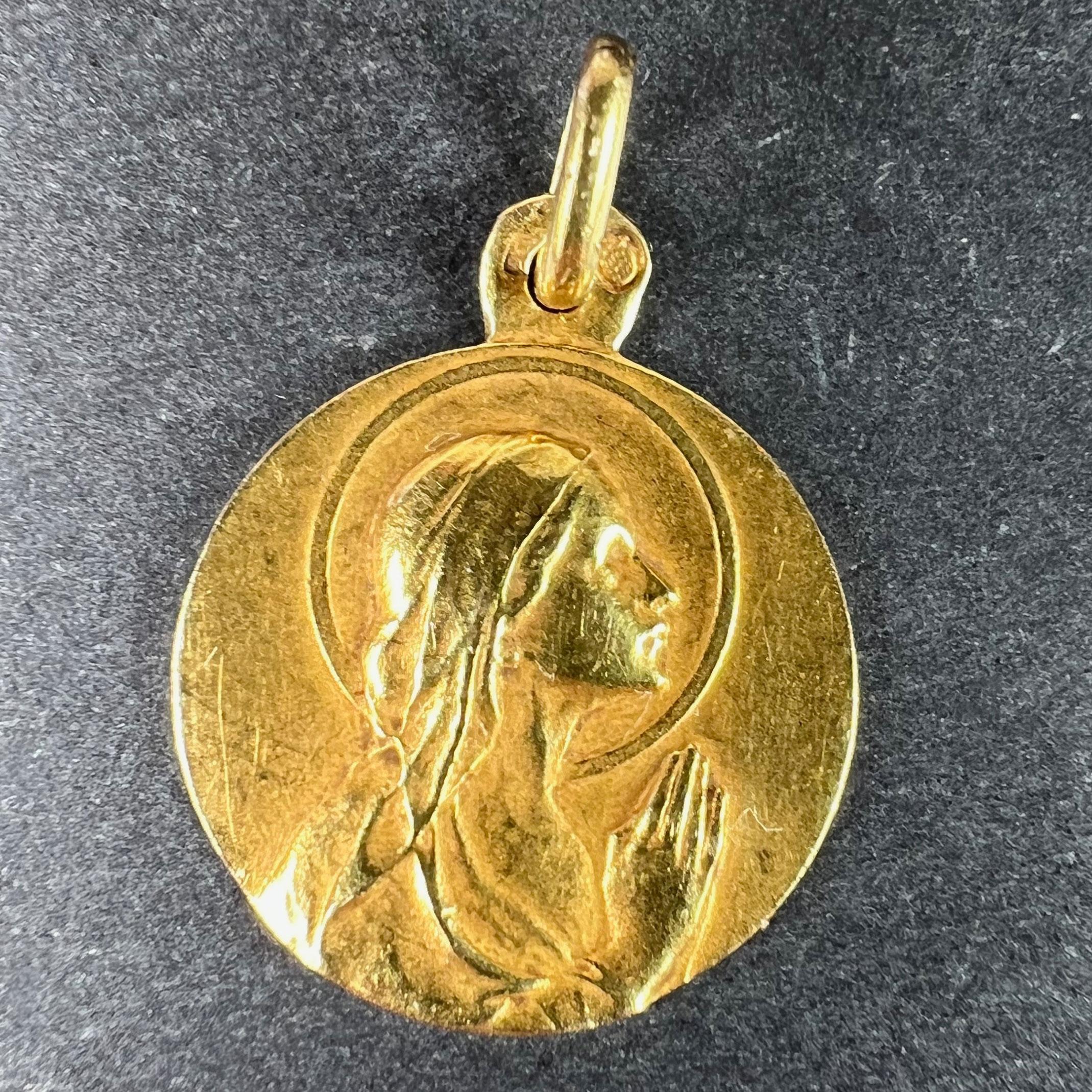 Un antico ciondolo francese in oro giallo 18 carati (18K) disegnato come una medaglia che raffigura la Vergine Maria di profilo, in preghiera, con un'aureola. Sul retro è inciso il monogramma JB / JB e la data 