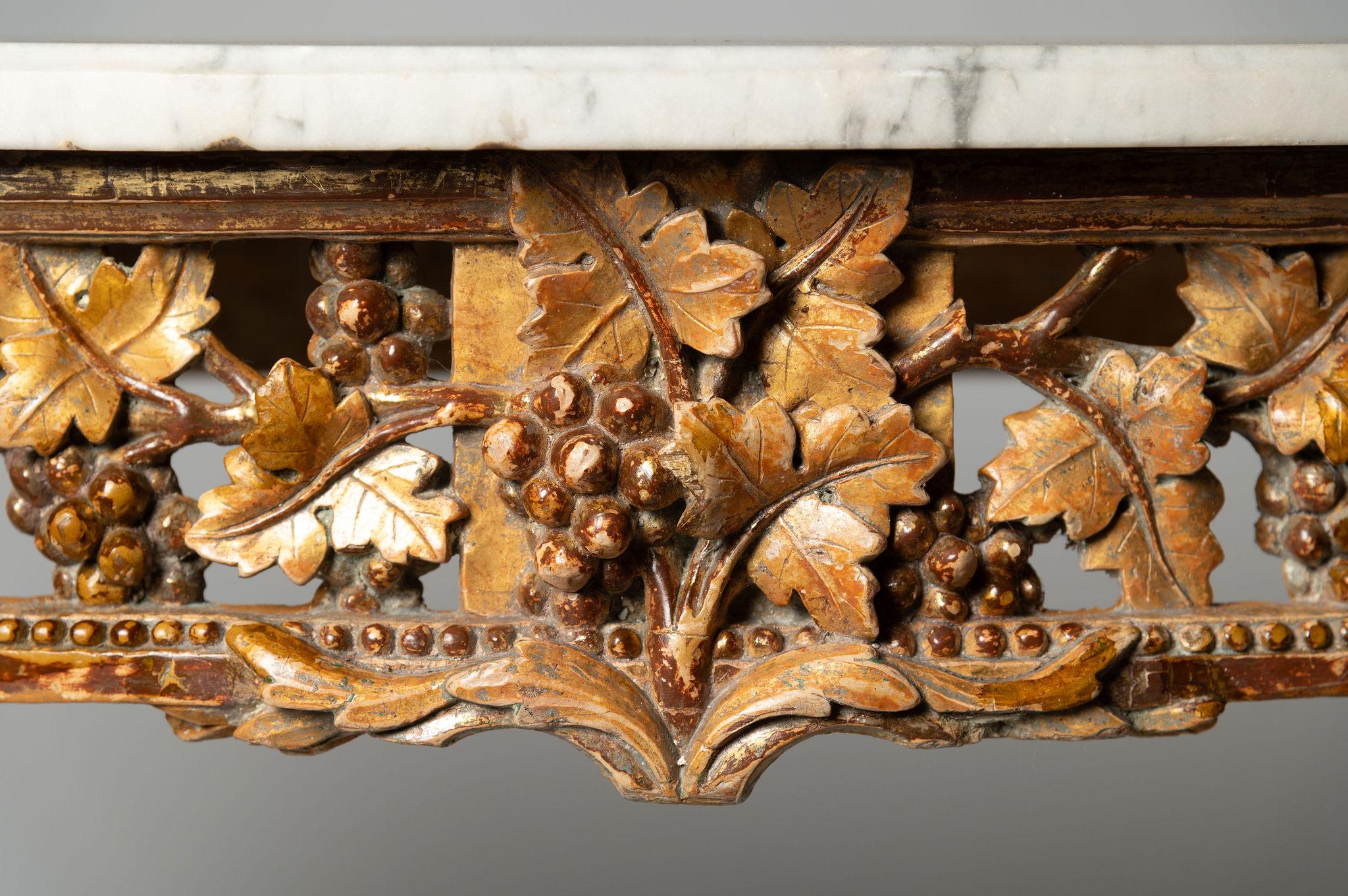 Exceptional 18th Century French console table, from the Louis XVI period in gilded finally carved wood, with openwork crosspieces of vine leaves and grapes. Original Carrara marble. Pretty original gilding. Light wear to the marble - as to expected.