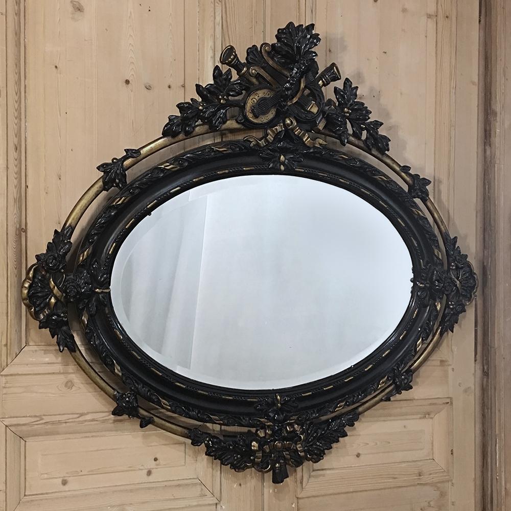 Créé dans une forme ovale inhabituelle orientée horizontalement, ce merveilleux miroir ovale Louis XVI français ancien du 19ème siècle présente des détails spectaculaires de haut en bas ! La couronne au centre du sommet présente des instruments de