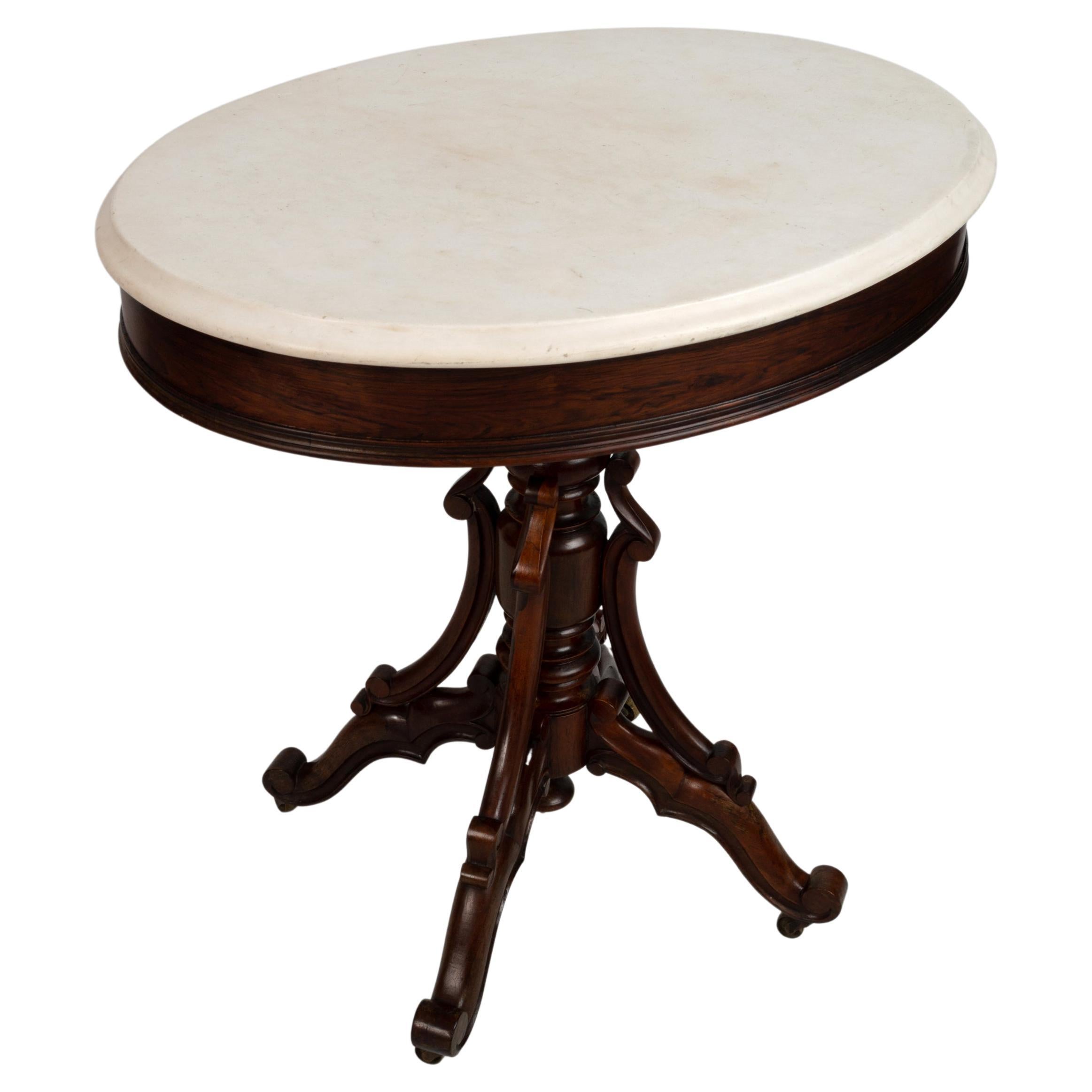 A French rosewood oval occasional table, 19th century, the white marble top with a moulded edge, over a turned stem, on four scrolling legs, joined by scrolling brackets, terminating in brass castors.

74cm high x 73cm wide x 53cm deep.

In