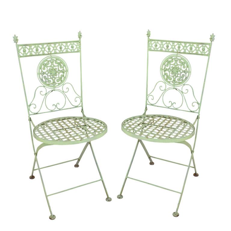 A pair of two antique French metal folding garden or patio chairs. This set of chairs will be an excellent addition to a patio, porch, or garden dining and entertaining. Each chair folds and is decorated with ornate metal designs at the top and