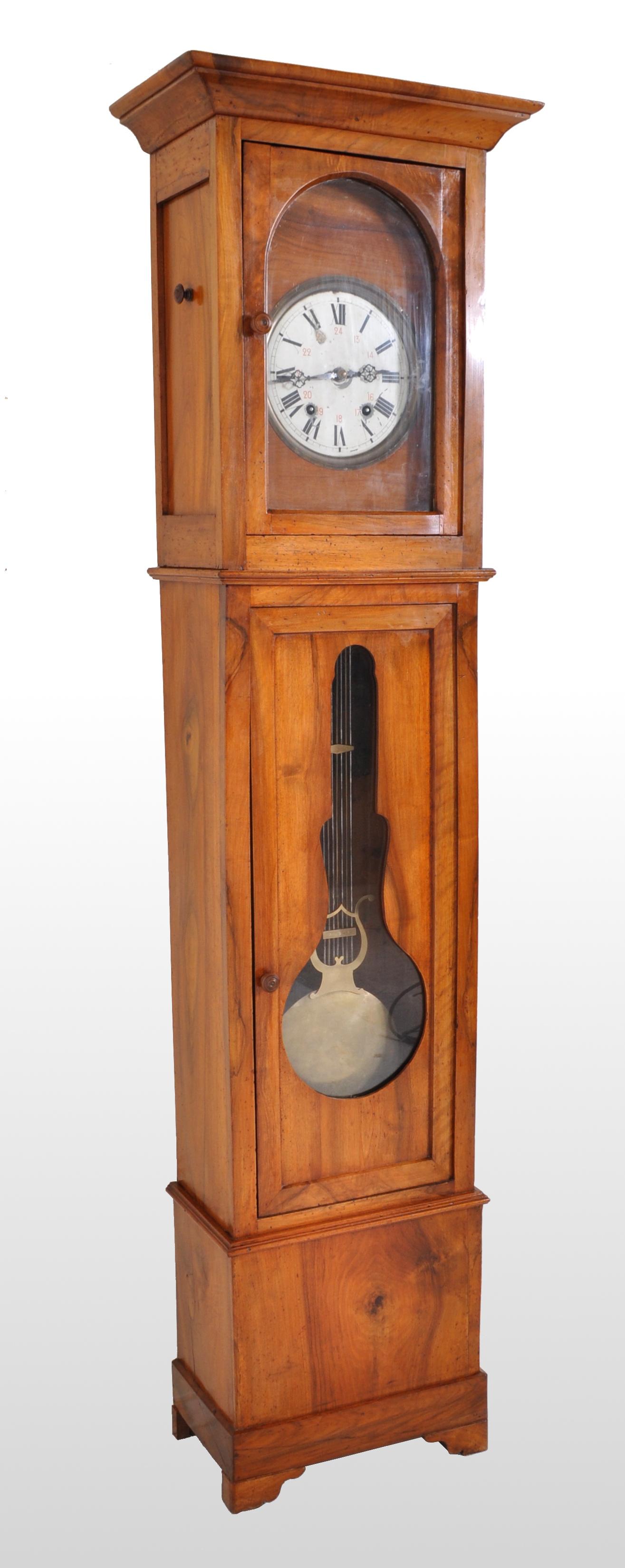 Pendule comtoise/morbier française ancienne de 8 jours en merisier:: vers 1820. L'horloge possède un cadran en émail blanc avec des chiffres romains noirs:: une porte simple à l'avant exposant un pendule décoratif en laiton:: le boîtier reposant sur