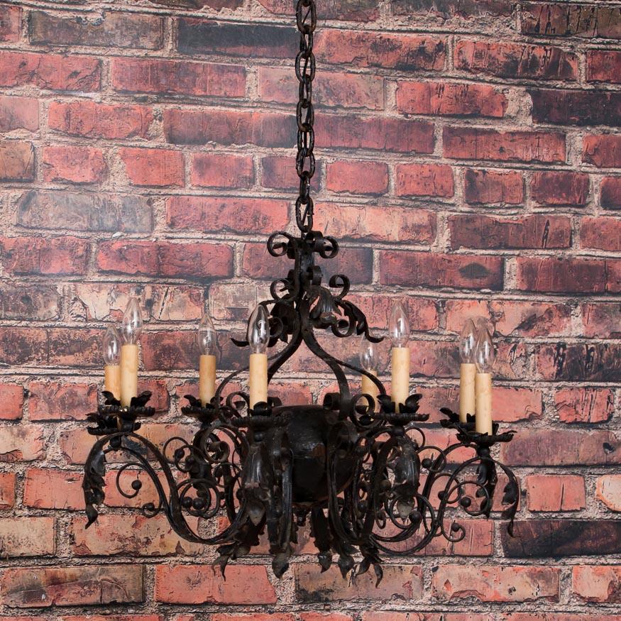 This unique antique French wrought iron chandelier has an organic feel with its eight scrolled arms and applied leaf details. The eight ornate arms radiate out from a centre globe, each with a single light and candle cover resting on a floral drip
