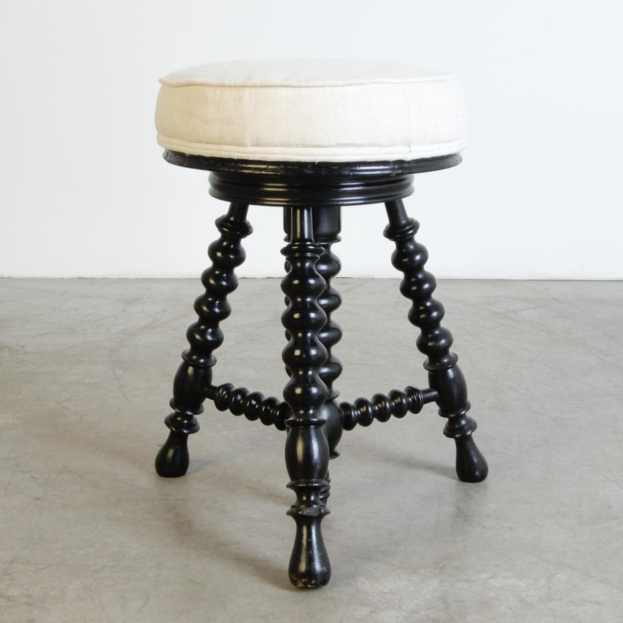 A minimal and decorative French design from circa 1900. Wooden turned legs support a round upholstered seat, rotating up and down with a spinning mechanism hidden inside a central column. Dramatic and reserved black with a great vintage patina,