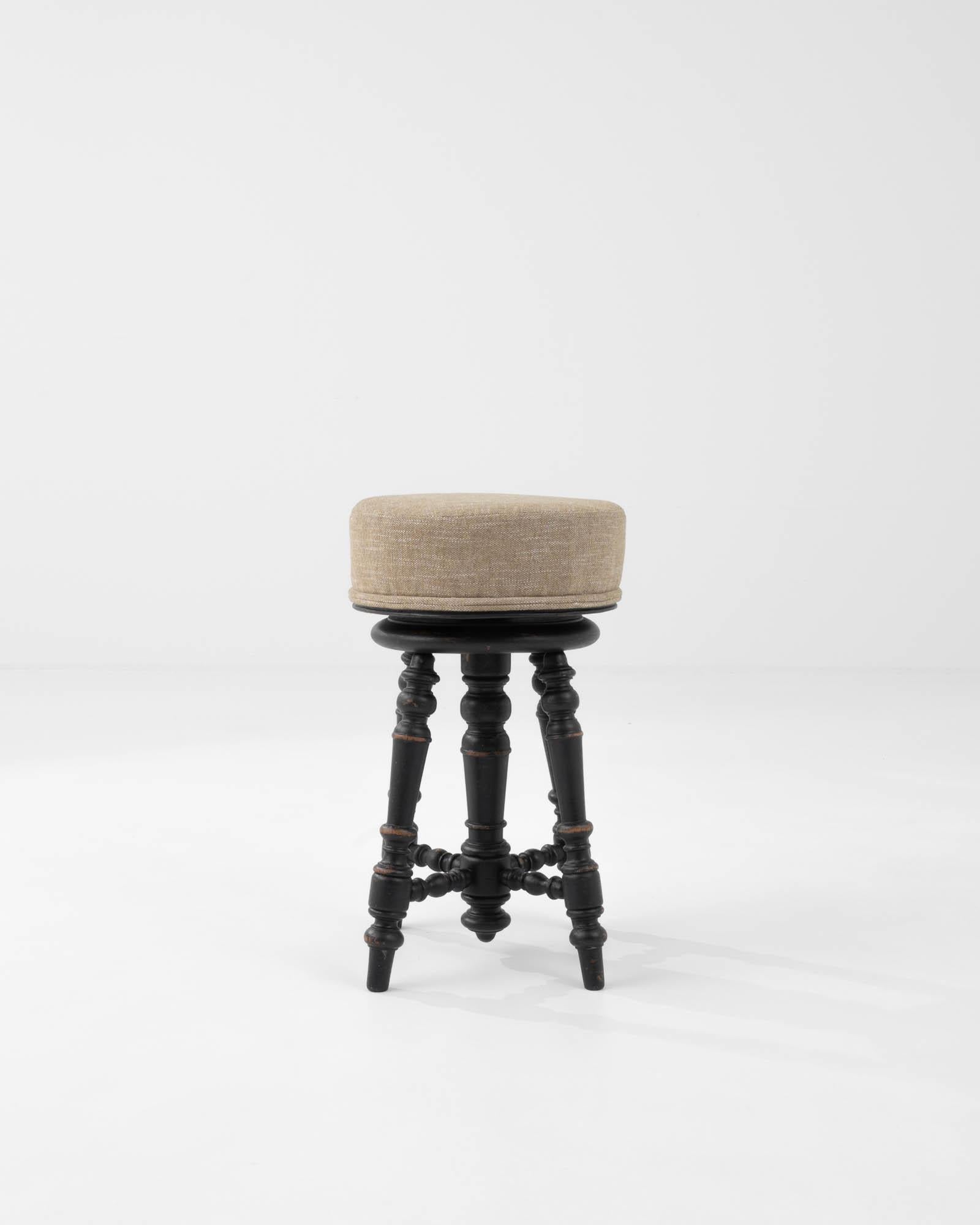 A minimal and decorative French design from circa 1900. Wooden turned legs support a round upholstered seat, rotating up and down with a spinning mechanism hidden inside a central column. The tone of the wood, a gently worn russet hue, contrasts