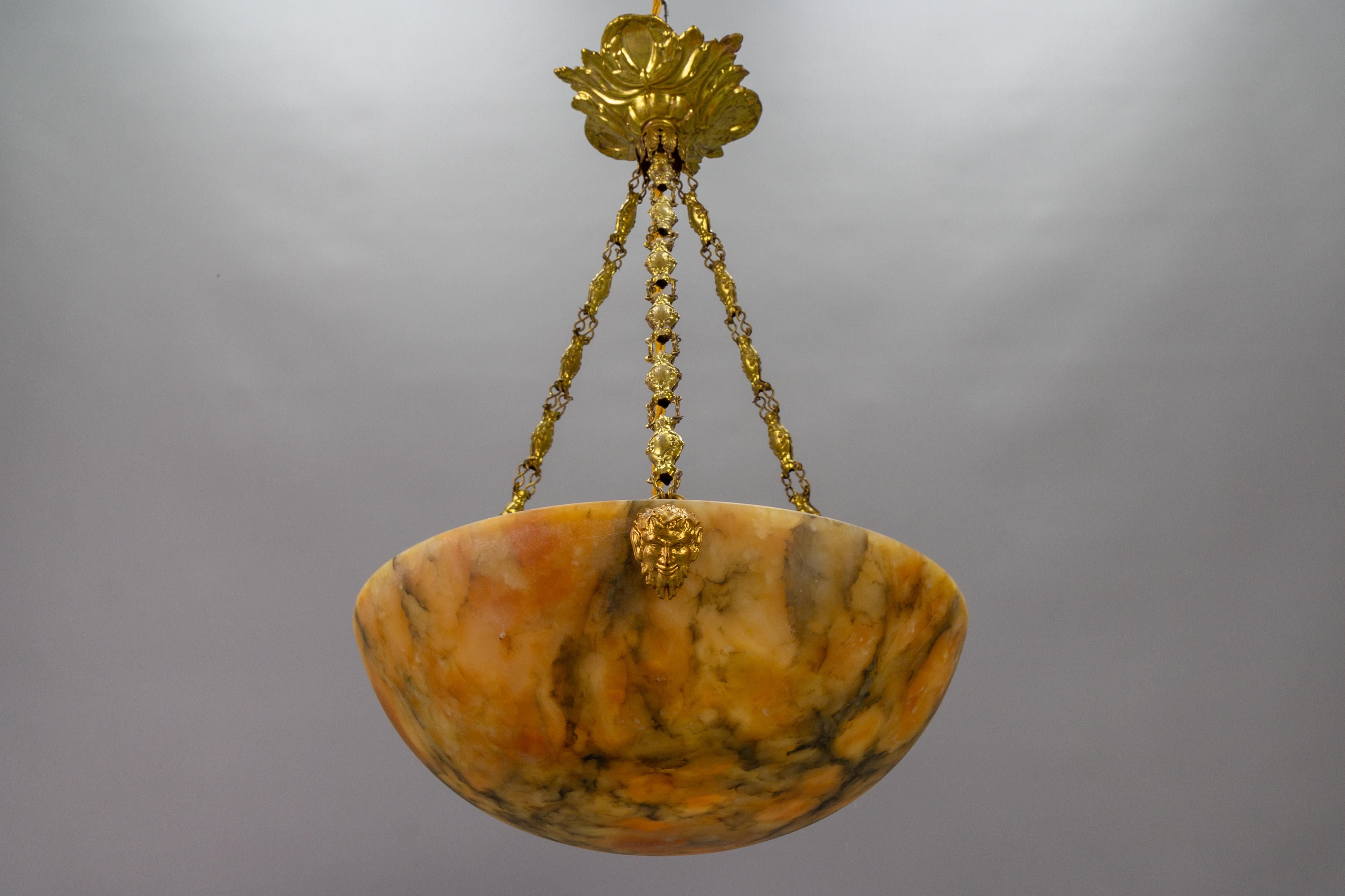 An absolutely adorable French pendant light featuring an alabaster shade in a lovely orange hue with gray and cream veining. The lampshade - bowl is suspended from three ornate brass chains, which attach to the dome with finely made satyr head brass