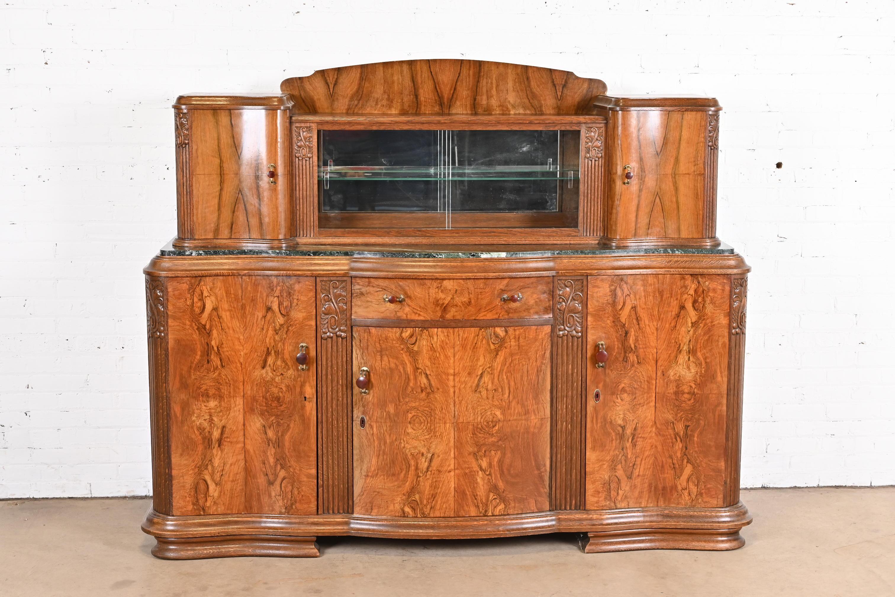 An outstanding French Art Deco sideboard, credenza, or bar cabinet

In the manner of Jules Leleu

France, circa 1930s

Carved oak, with gorgeous book-matched burled walnut front, green marble top, and original bakelite and brass hardware.
