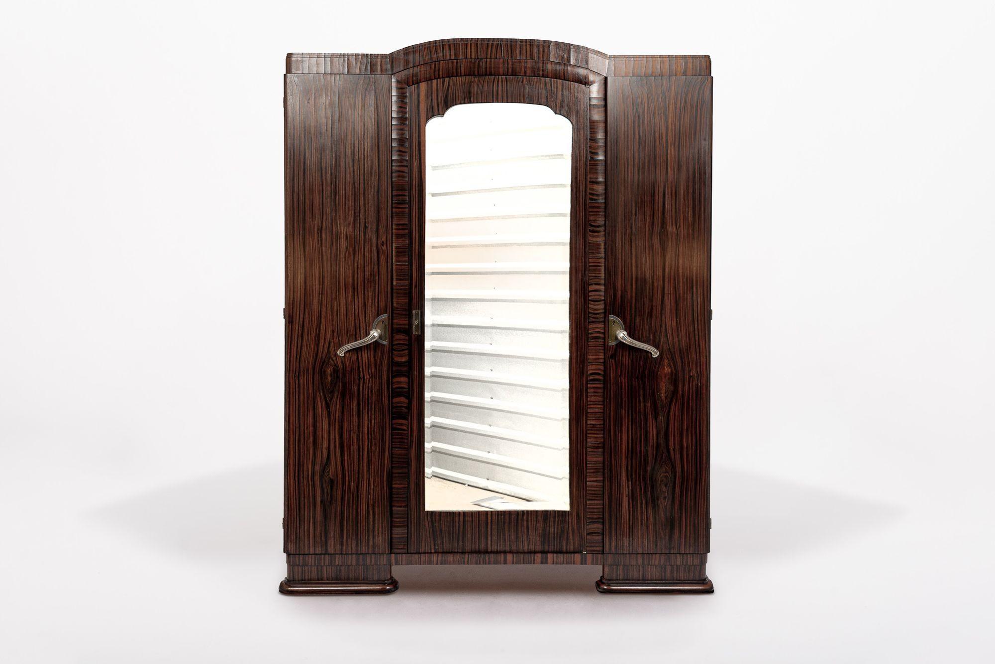 Dieser exquisite antike Art Deco Kleiderschrank aus Holz wurde um 1940 in Frankreich hergestellt. Dieser Hochschrank wurde in tadelloser Handarbeit aus Massivholz und Makassar-Ebenholzfurnier gefertigt und besticht durch seine tiefe, dunkelbraune