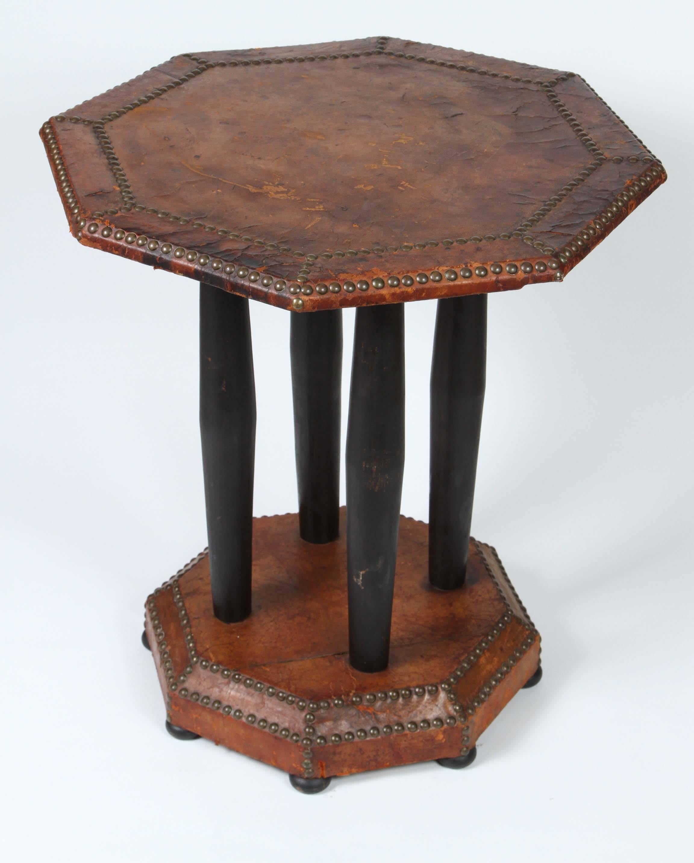 French Art Deco distressed leather side bistro table.
Unique shape antique octagonal wood table with leather wrapped top with studded detail that sits on four tapered black pedestals that connect to a smaller octagonal base also covered in a studded