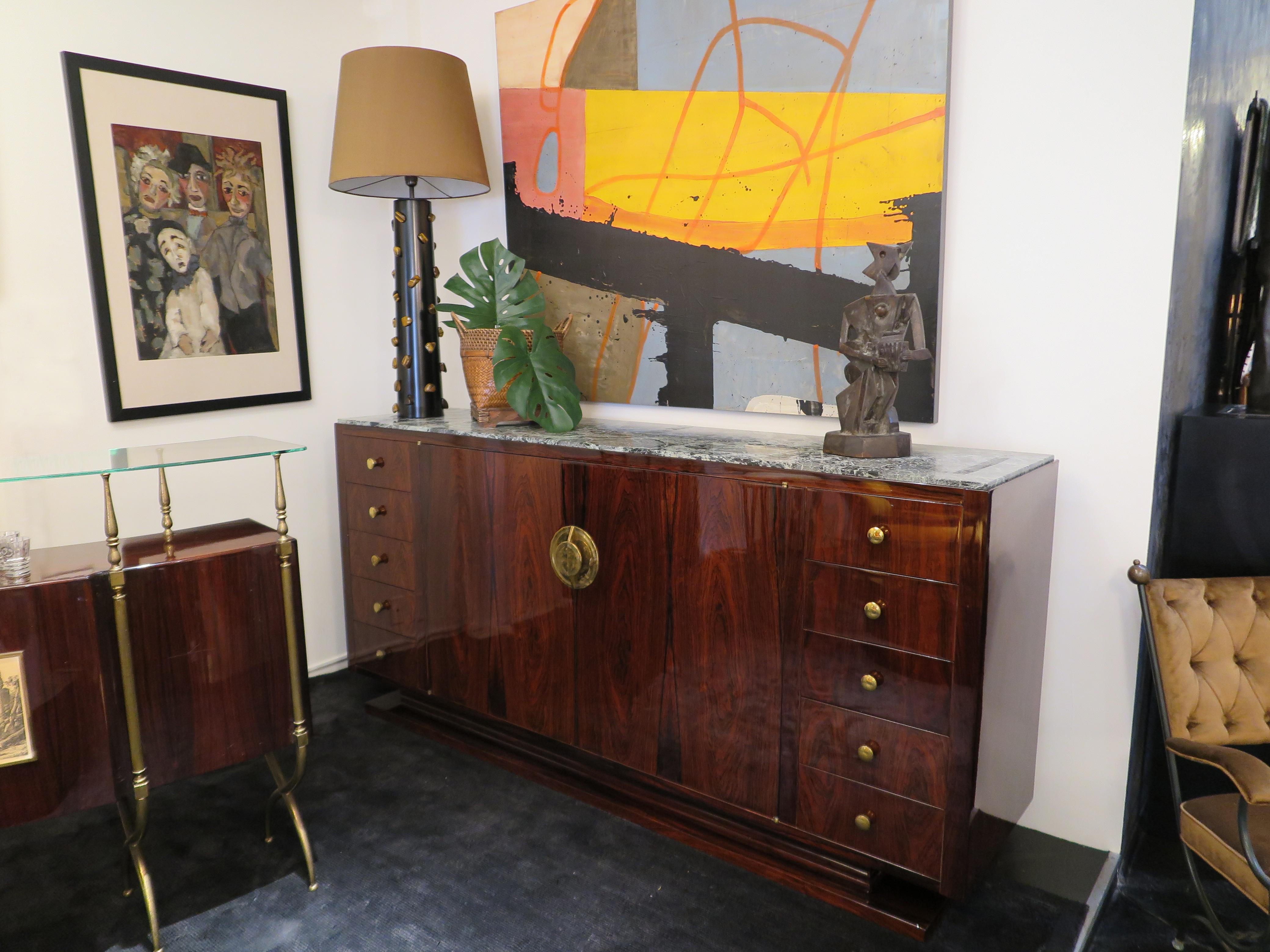 This grand French Art Deco sideboard is crafted in Rosewood and is newly refinished in high gloss. Each side showcases five drawers with two cabinet doors in the center. The middle doors are highlighted by a rounded hardware pull in brass. The base
