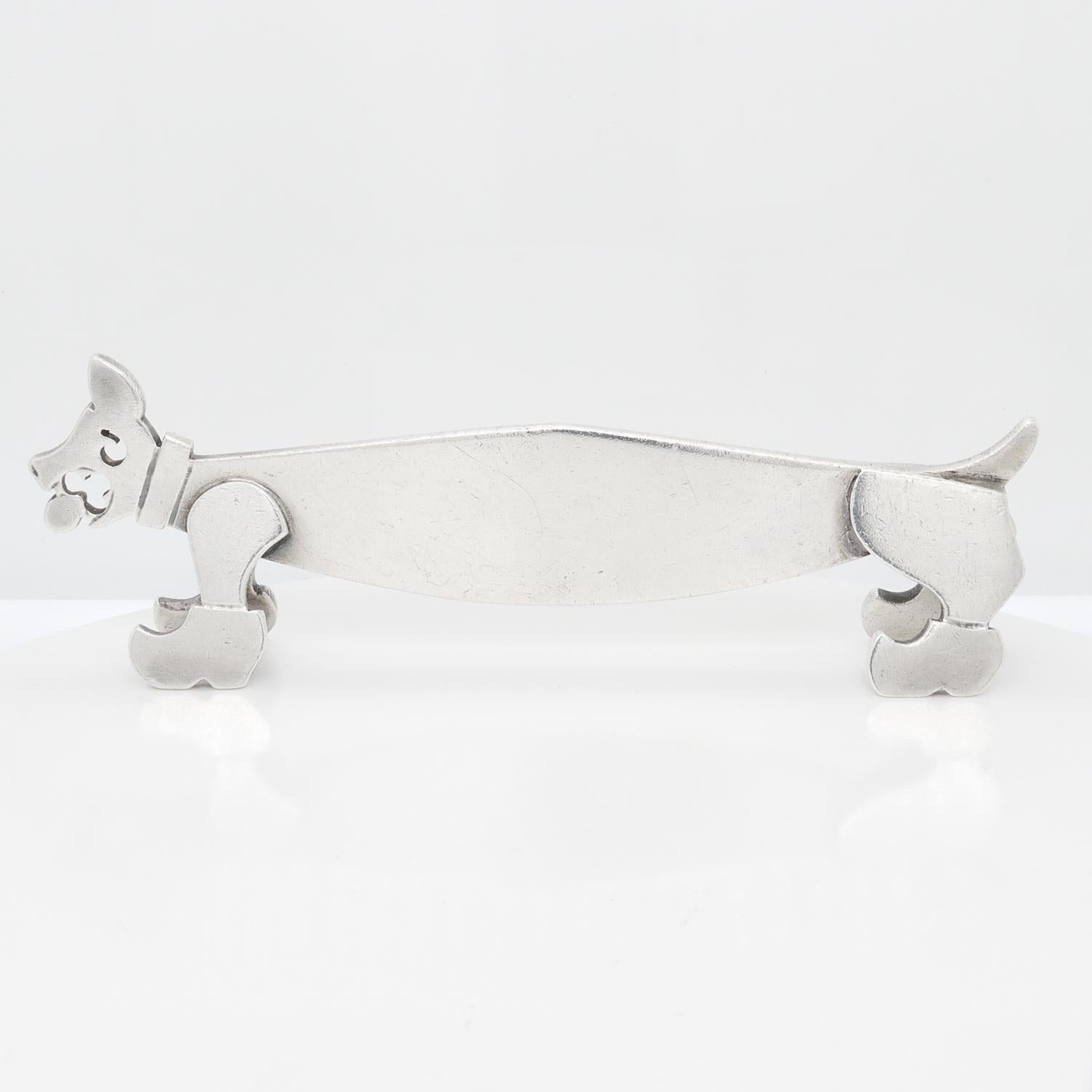 A fine, signed French Art Deco knife rest.

In French second standard silver.

By Louis Mathey, the renowned French Art Deco silversmith.

In the form of a flat cut dog body with soldered legs and clogs (or klompen shoes). The dog has a raised tail,