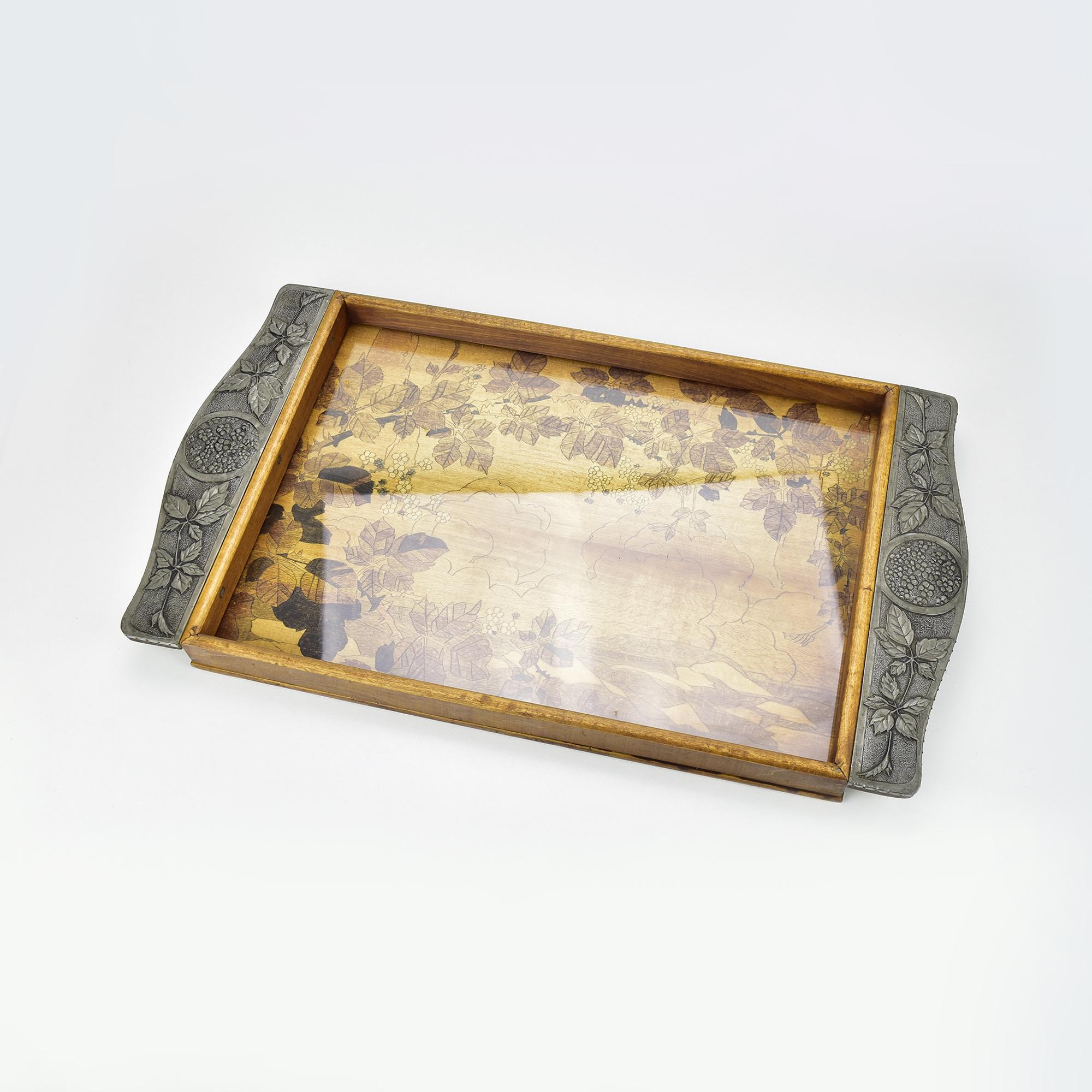Questo squisito vassoio da portata francese antico incarna l'eleganza dell'epoca Art Nouveau. Realizzato in legno dai toni caldi, presenta manici in peltro delicatamente ripassati e ornati da intricati motivi floreali e di foglie, che ricordano i