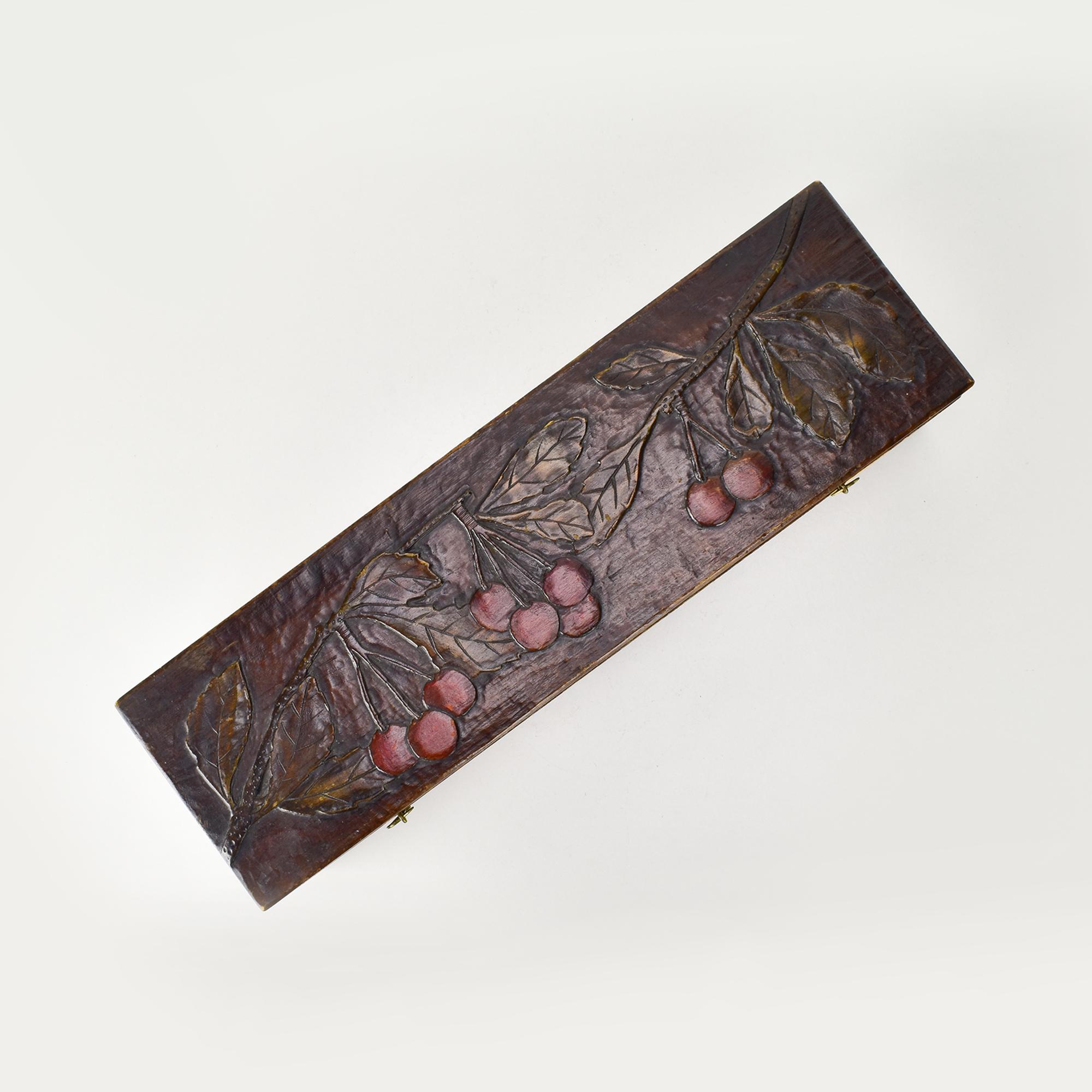 Cette exquise boîte en bois Art nouveau présente un motif de cerise magnifiquement sculpté sur son couvercle, capturant l'élégance organique typique du début du 20e siècle. Le travail en relief complexe met en valeur les courbes et les détails