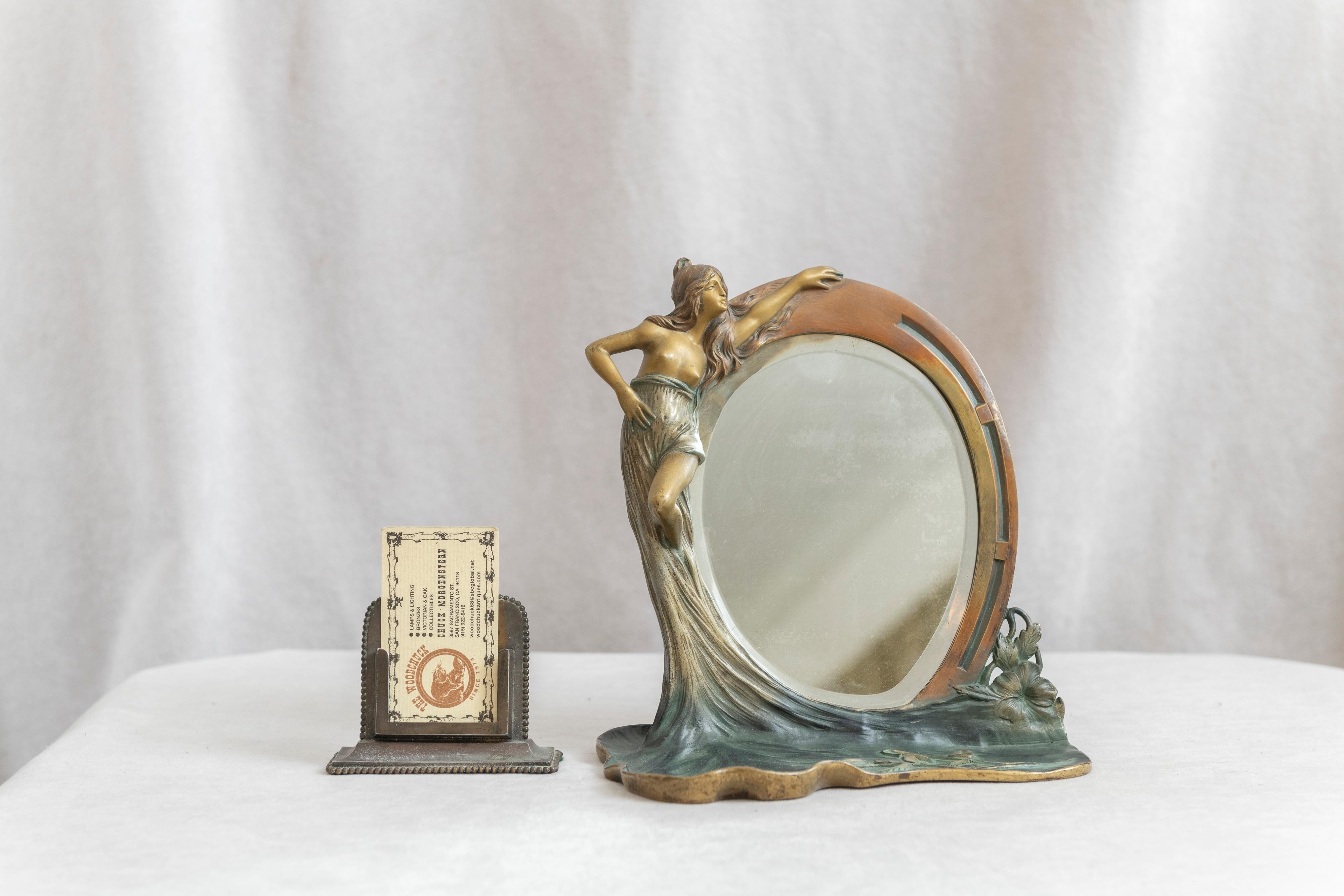 Un bel exemple de miroir figuré art nouveau en bronze. Une jeune femme tenant un miroir biseauté avec une zone plate en dessous couverte de fleurs. Nous avons particulièrement aimé cette zone plate pour l'attention portée aux détails des fleurs, et