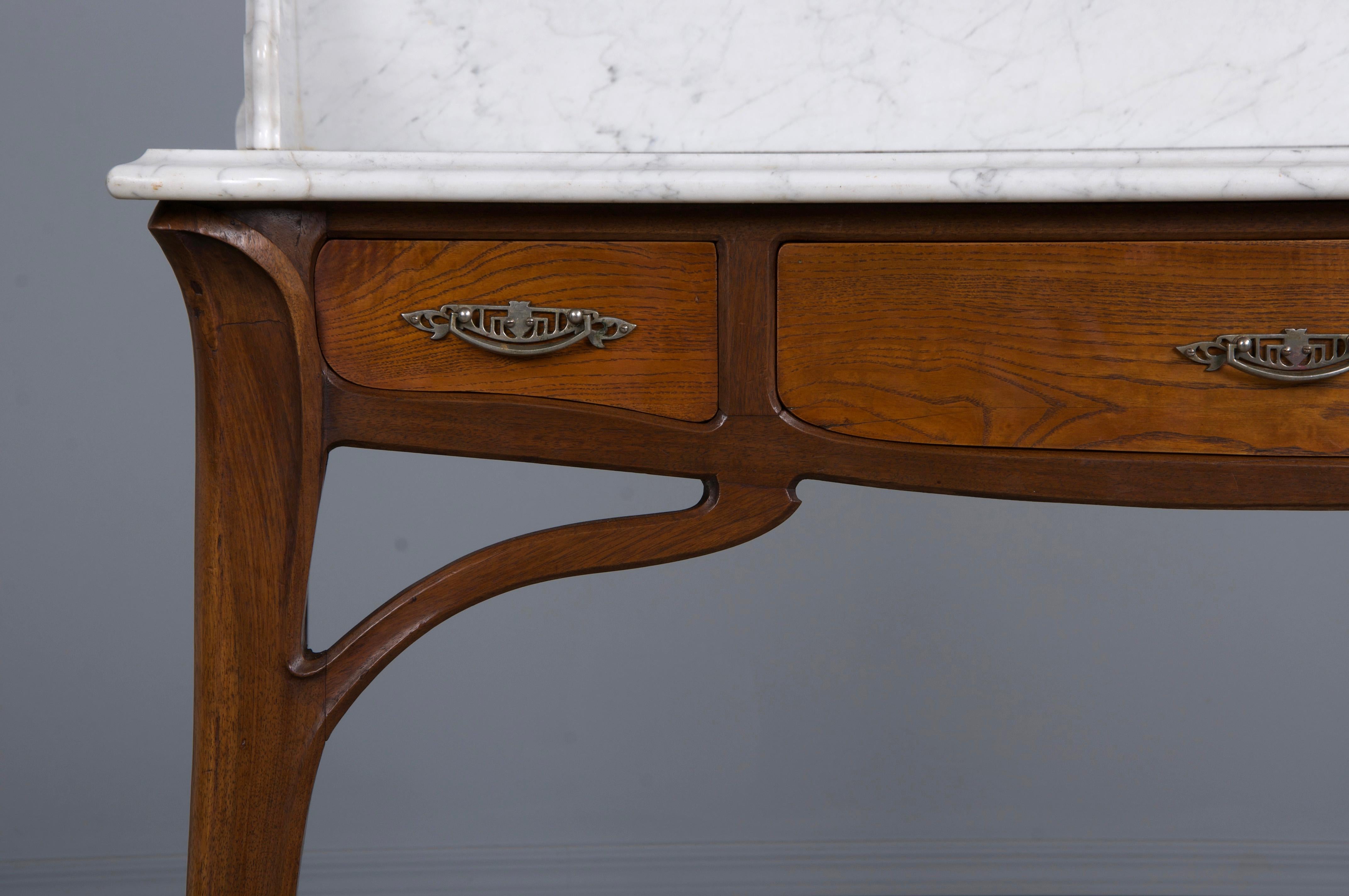 An exquisite 1890s French Art Nouveau wash table or vanity, sourced directly from Provence, France. Expertly hand-carved from solid oak, it features a stunning scalloped white Carrara marble top with delicate light gray veins and a single shelf. The