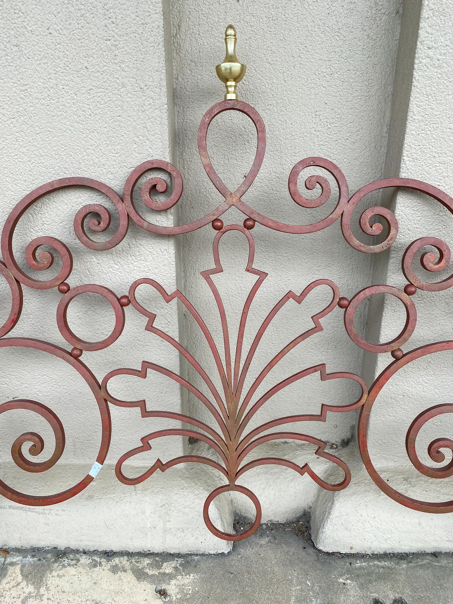 This stylized iron panel is painted in a crimson finish with turned brass finials. The piece dates to 1910 and is Art Nouveau in style. The back of the panel has three metal brackets from which this piece can be mounted to a wall, imagine this as a