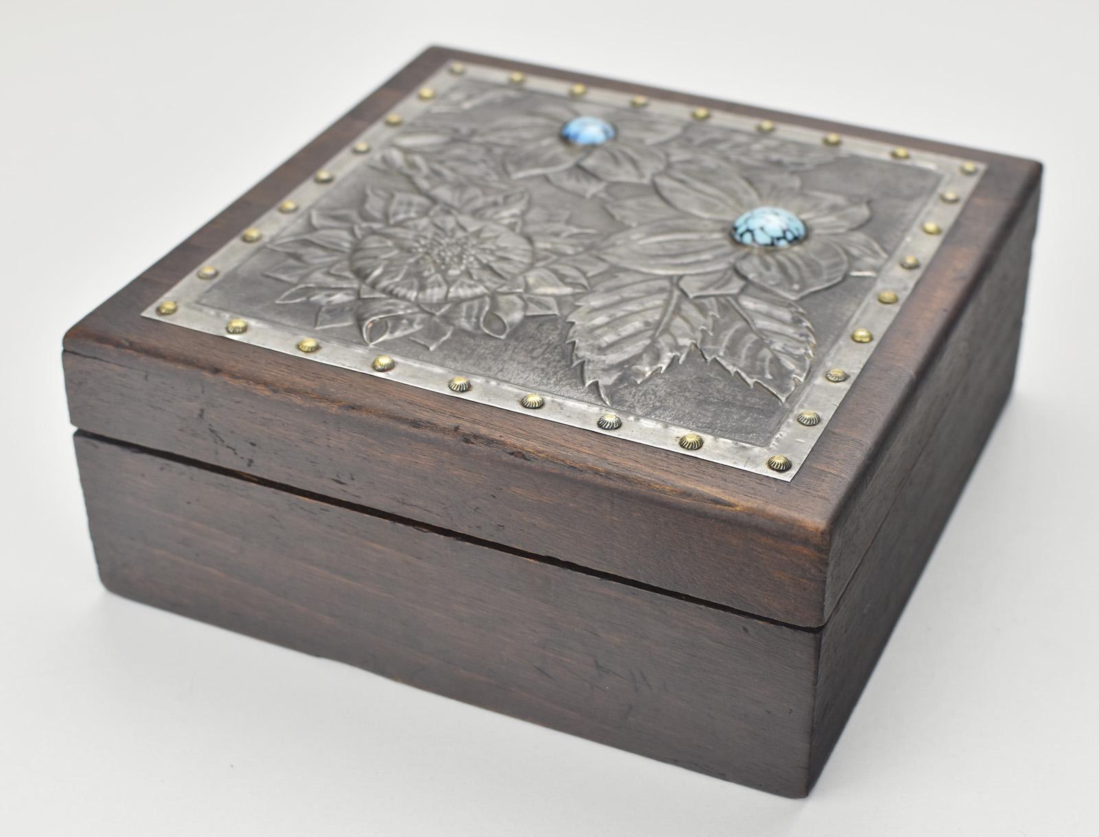 Esta exquisita caja de baratijas Art Nouveau francesa tiene una tapa de estaño repujado con intrincados motivos florales, dentro de un robusto cuerpo de madera. El detallado diseño muestra flores y hojas finamente trabajadas, acentuadas por dos