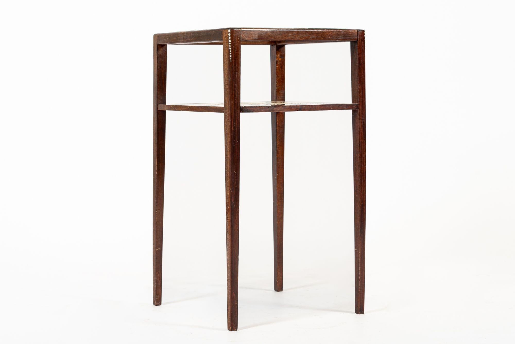 Cette petite table d'appoint ou de chevet décorative en bois d'acajou est datée des années 1900-1910. Cette exceptionnelle petite table artisanale présente d'élégantes proportions carrées avec de hauts pieds fuselés et un plateau à deux niveaux