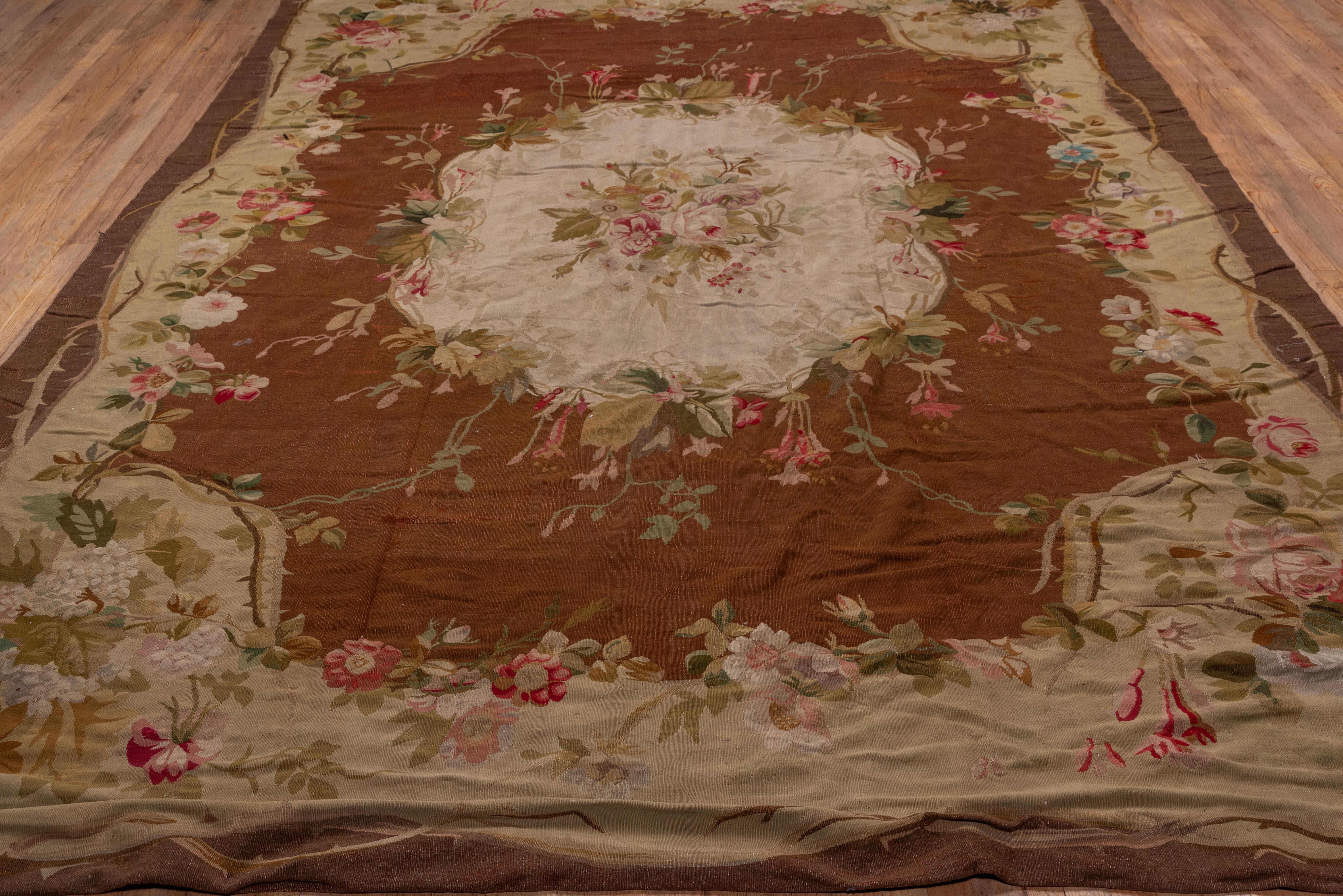 A gently undulating wide ivory border with roses, thorny stems and leaves surrounds the red field which is centered by a large lightly lobed medallion sprouting a garden of small posies and centered by a rose bouquet. This tapestry woven French