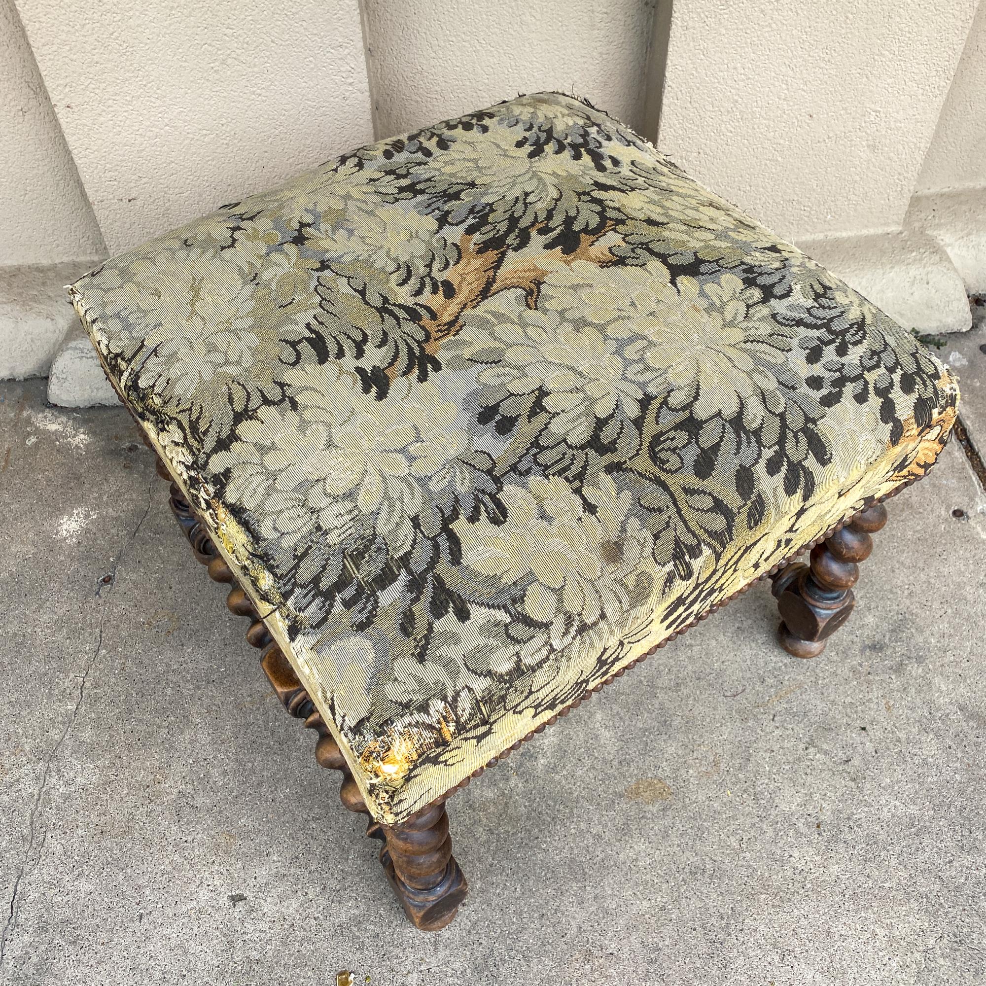 This antique French ottoman has several interesting details. The base is crafted of oak in a barley twist style with four twist legs joined at the sides and center with coordinating supports. The top of this piece is upholstered with an embroidered
