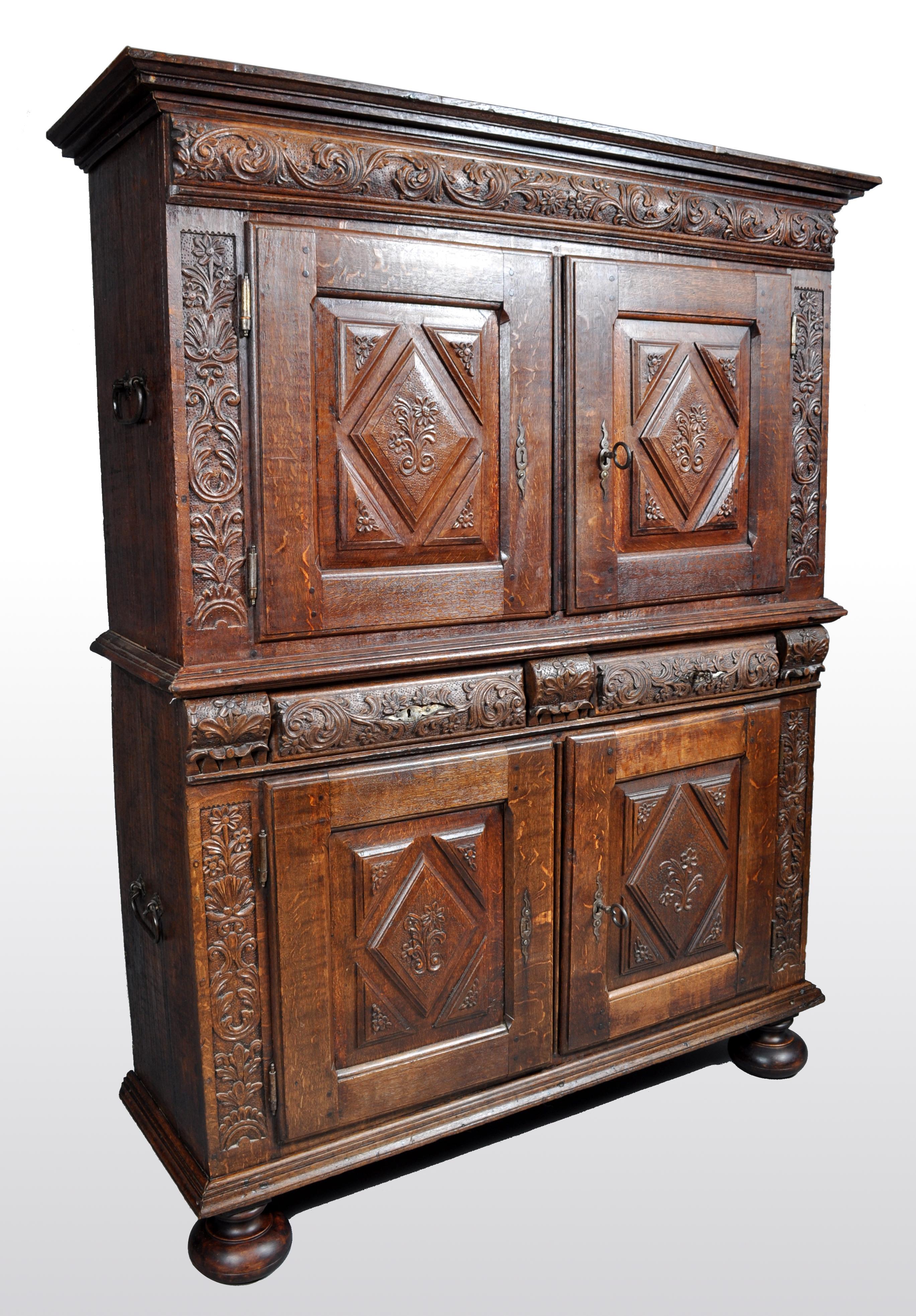 Antique French baroque carved oak court cabinet, circa 1750. The cabinet in two parts and having cast iron carrying handles to the top and the base. The cabinet having a stepped cornice with a carved foliate frieze below, the top and base having a