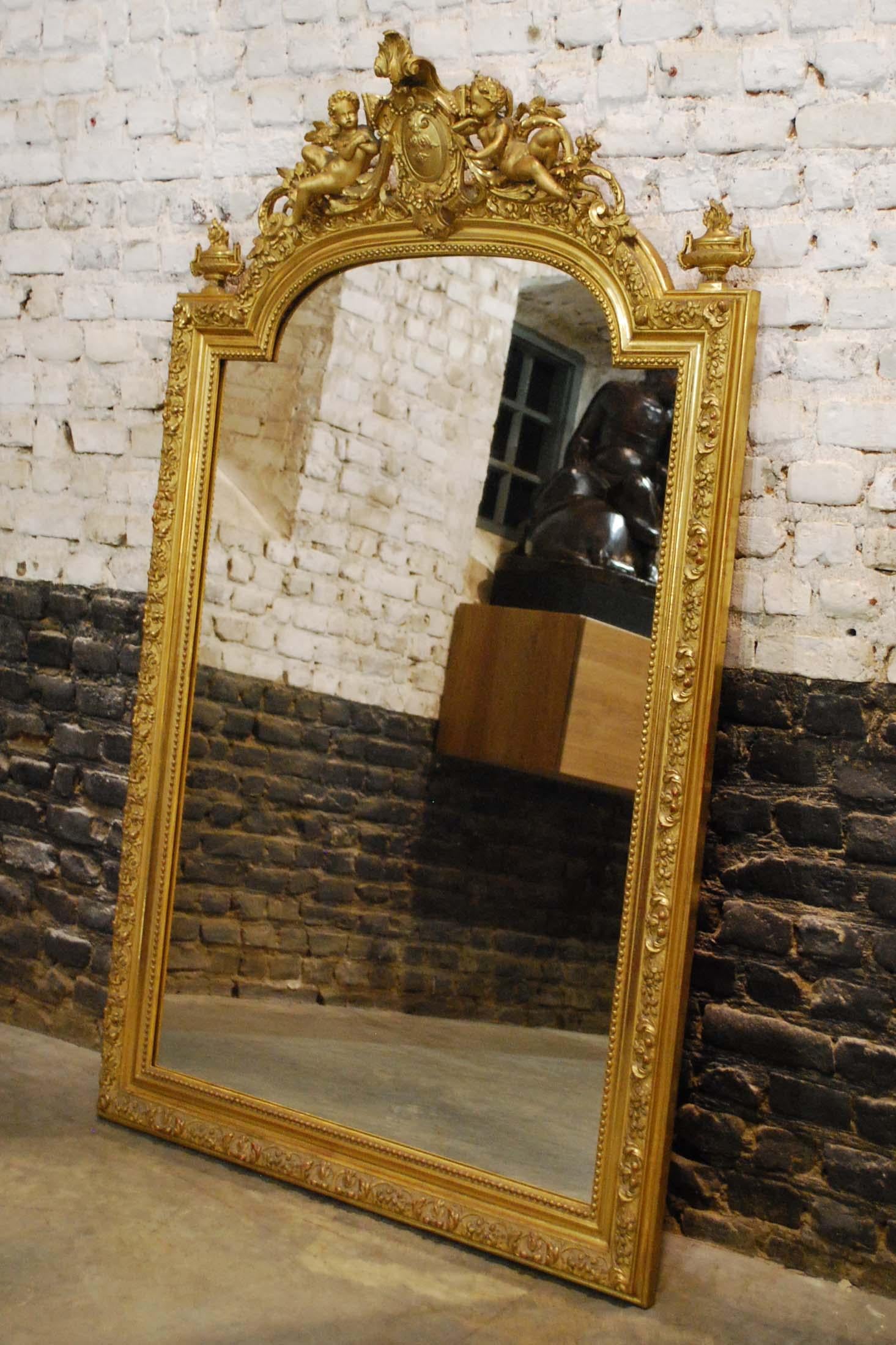 Ce beau miroir baroque doré est fabriqué en France, vers 1850. 
Le cadre a un sommet arqué et est enrichi de décorations complexes. Le miroir présente une crête ornée d'un médaillon central flanqué de deux anges ou putti et d'éléments acanthes et