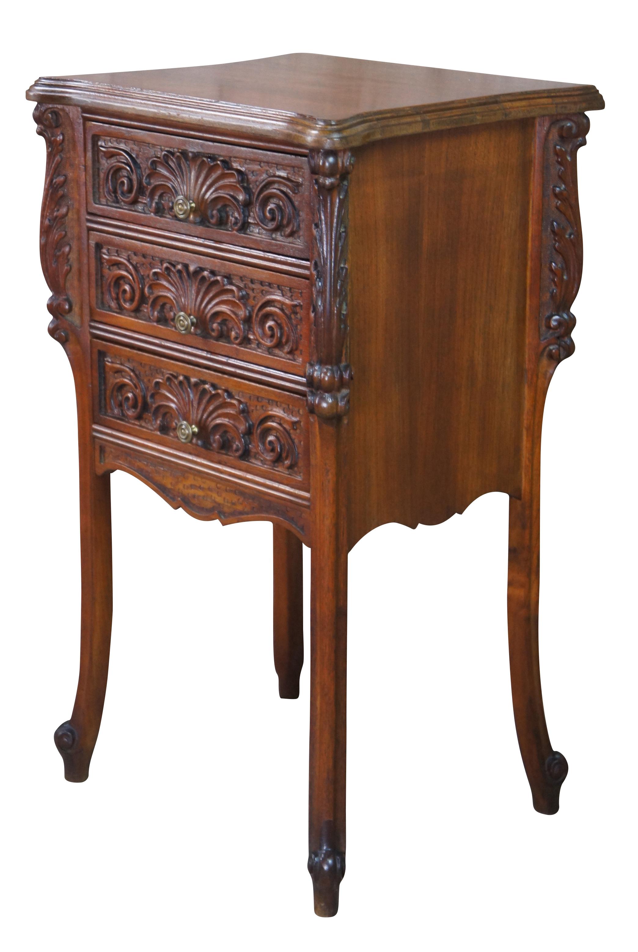 Antique French nightstand or side table. Made of walnut featuring three drawers with shell and catouche carvings between thick acanthus accents, and cabriole legs leading to scrolled feet. Measures: 27
