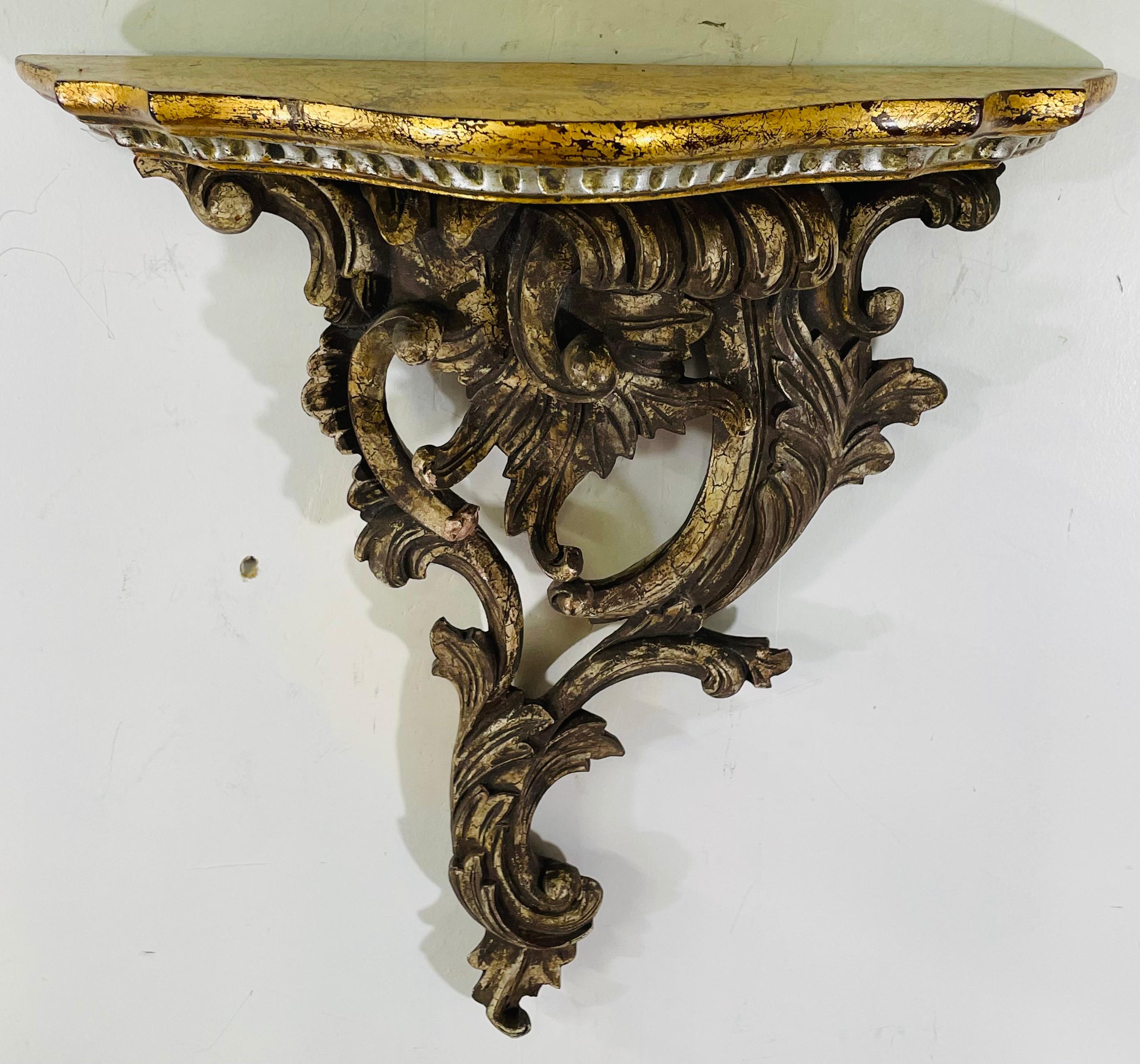 A pair of French Baroque style hand carved gesso and wood floral scroll design wall brackets featuring a scalloped gild painted shelving. This elegant pair of brackets will add style and sophistication any wall or space. 

Dimensions: 15