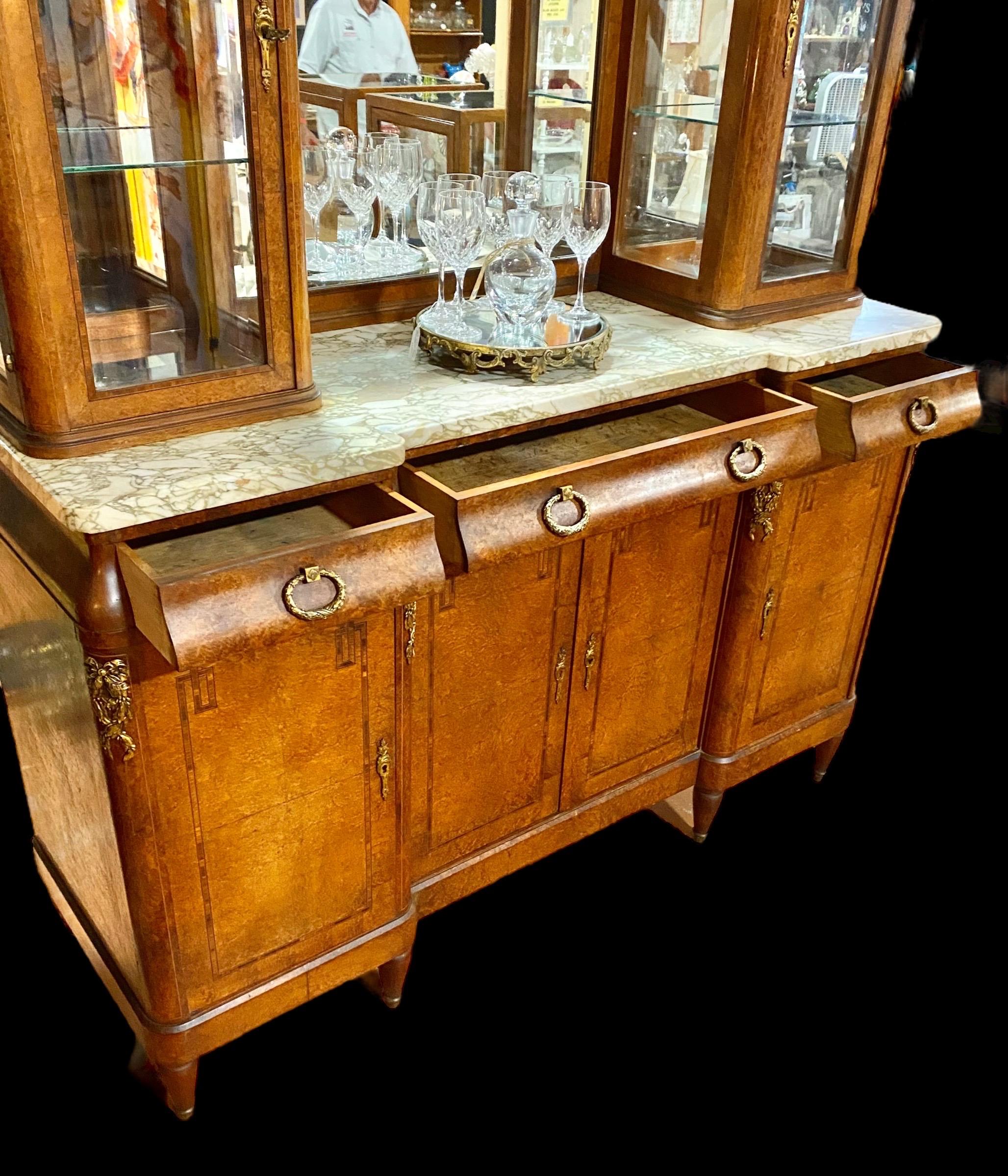 An outstanding antique French Beaux Arts gilded Ormolu Mounted Inlaid Carved Walnut and bird’s-eye maple marble top, 20th c., with a central arched wide beveled mirror, flanked by two wide beveled glazed cabinets, on a thick highly figured white