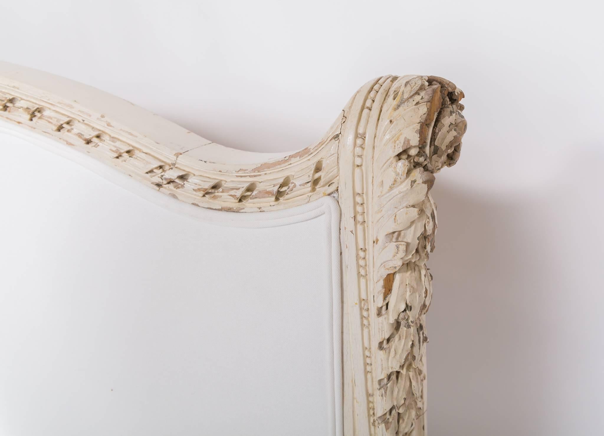 Ce magnifique lit français ancien du 19e siècle est habilement sculpté et présente une belle peinture blanche ancienne et une tapisserie en coton mélangé blanc sur le devant du lit. 