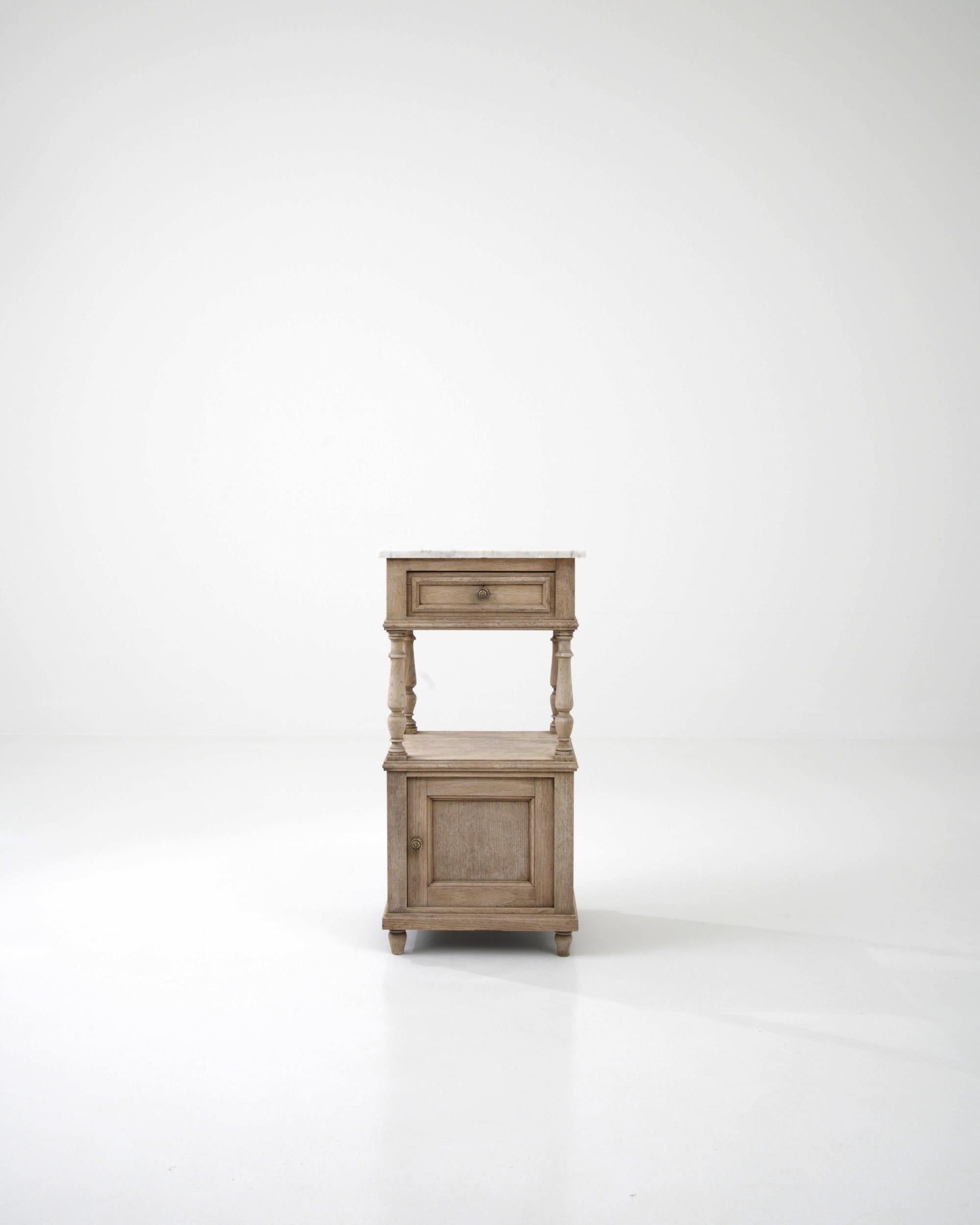 An oak night stand created in France circa 1900. Traditionally crafted, this subtly styled bedside table is adorned with a marble top, projecting a sense of calm and refined elegance. Cloudy gray veins drift through the ivory colored marble top