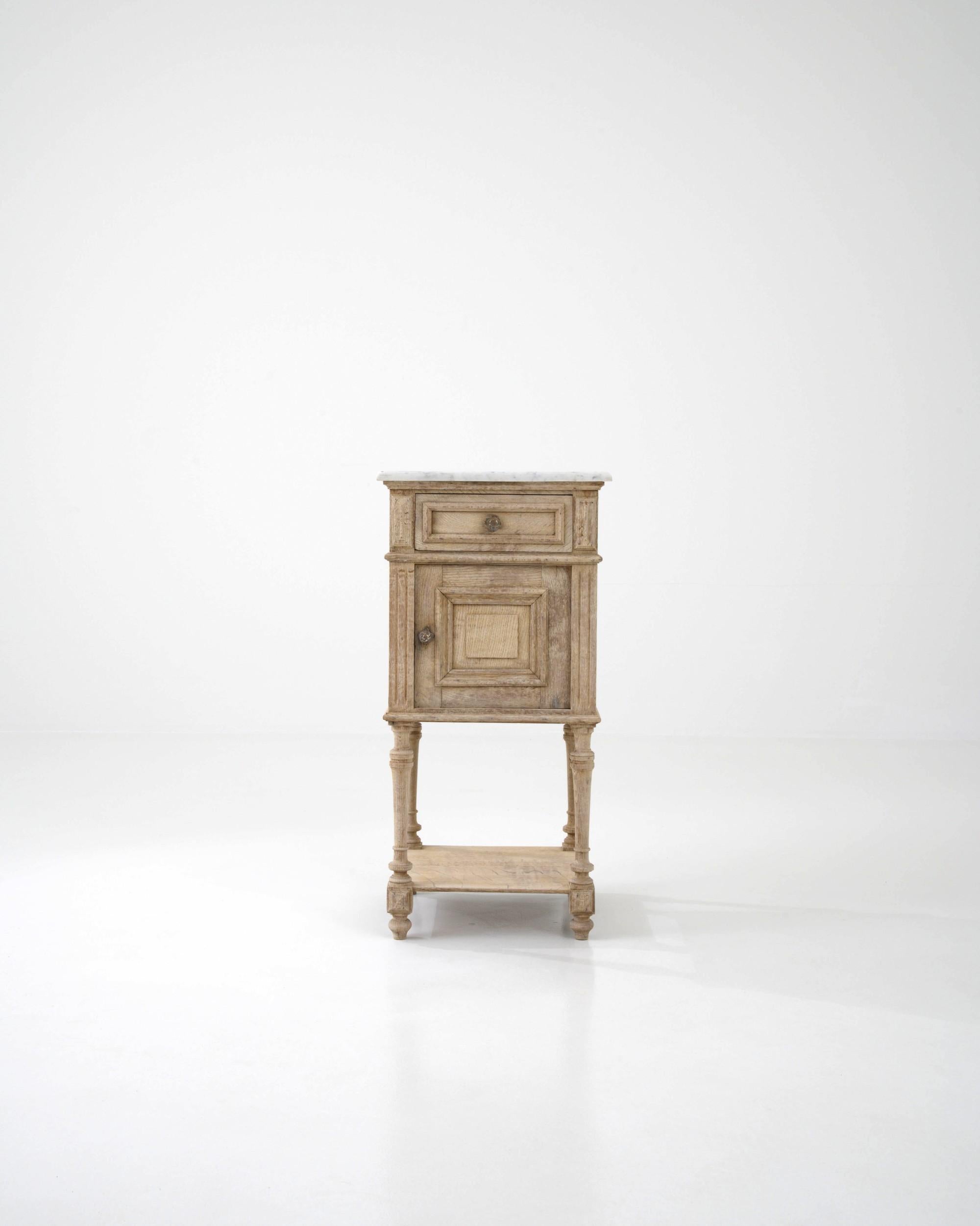 An oak night stand created in France circa 1900. Traditionally crafted, this subtly styled bedside table is adorned with a marble top, projecting a sense of calm and refined elegance. Cloudy gray veins drift through the ivory colored marble top