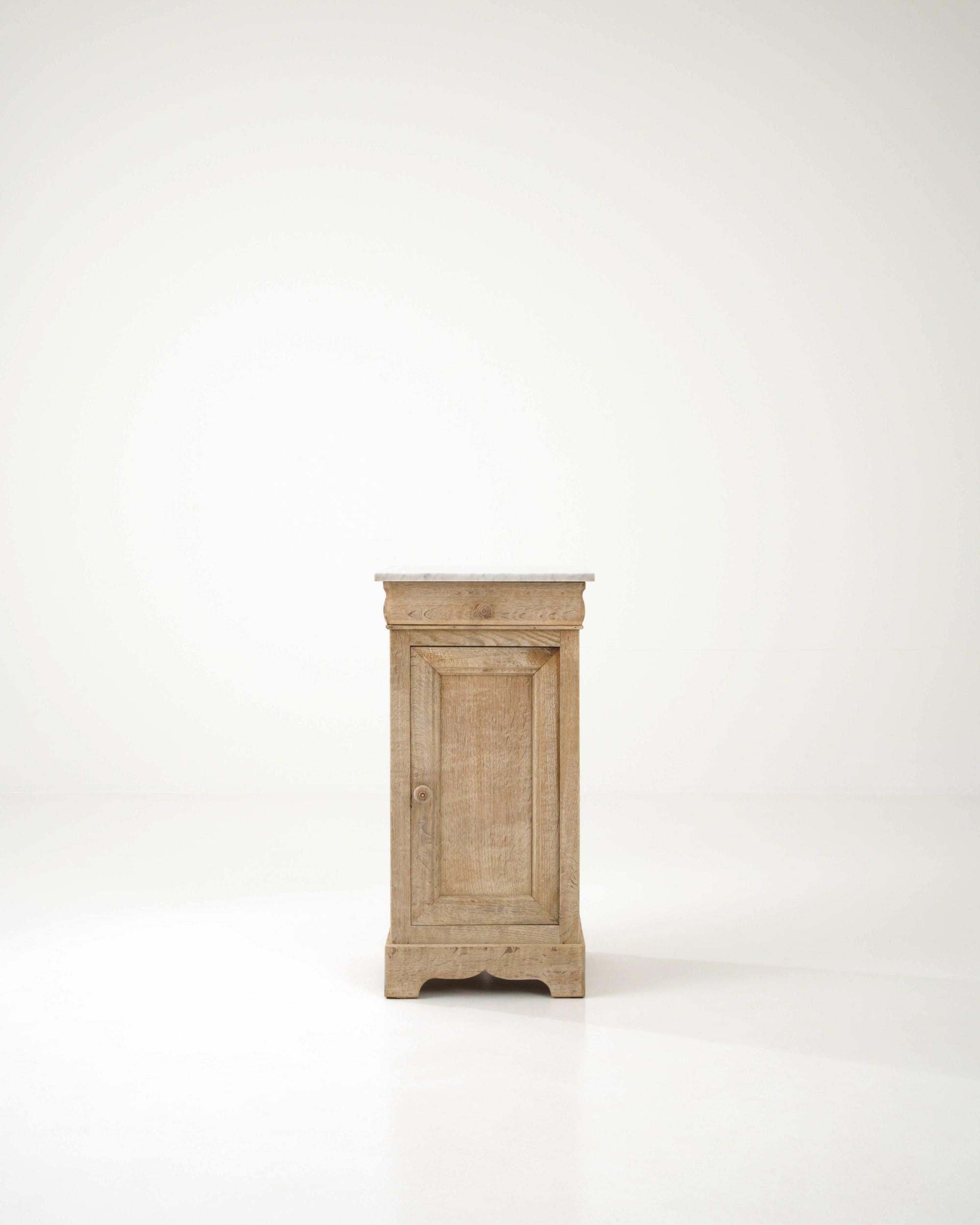 An oak night stand created in France circa 1900. Traditionally crafted, this subtly styled bedside table is adorned with a marble top, projecting a sense of calm and refined elegance. Cloudy gray veins drift through the ivory colored marble top