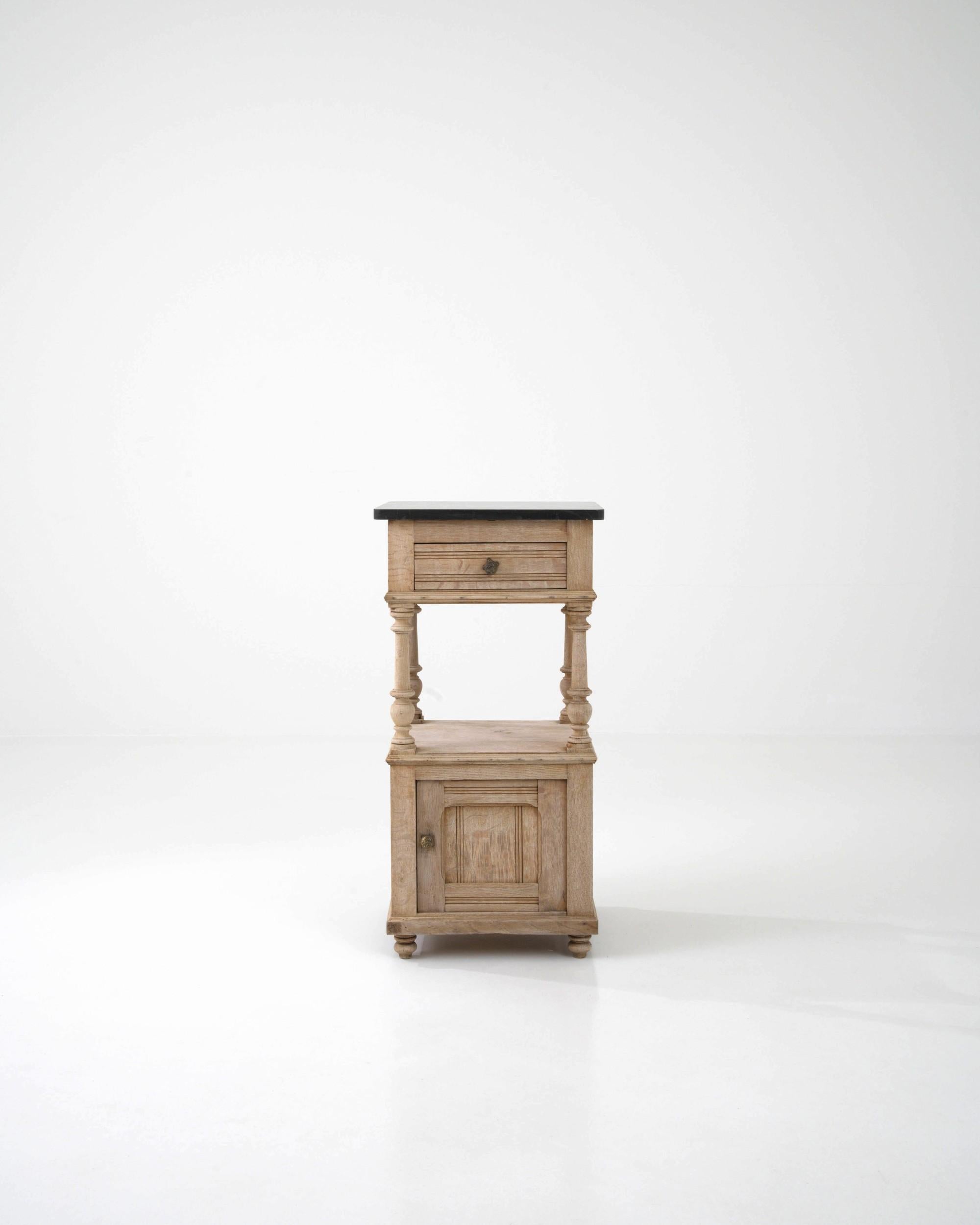 An oak night stand created in France circa 1900. Traditionally crafted, this subtly styled bedside table is adorned with a stone top, projecting a sense of calm and refined elegance. Cloudy gray veins drift through the dark slate colored stone