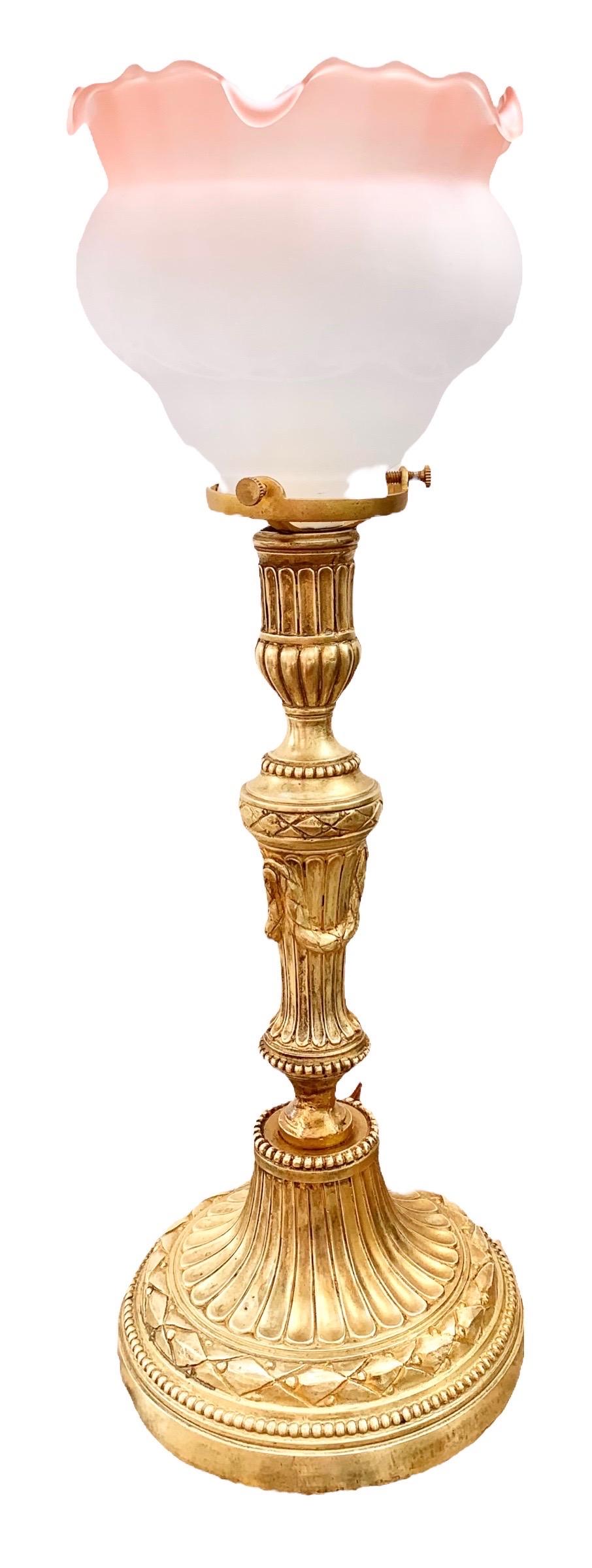 An antique French Belle Epoche gilt bronze candlestick lamp having a fine reproduction, hand made, frosted, ruffled and etched glass shade with a tinge of pink. Beautiful detailed with garlands, reeding and incised leaf borders.

It casts such an