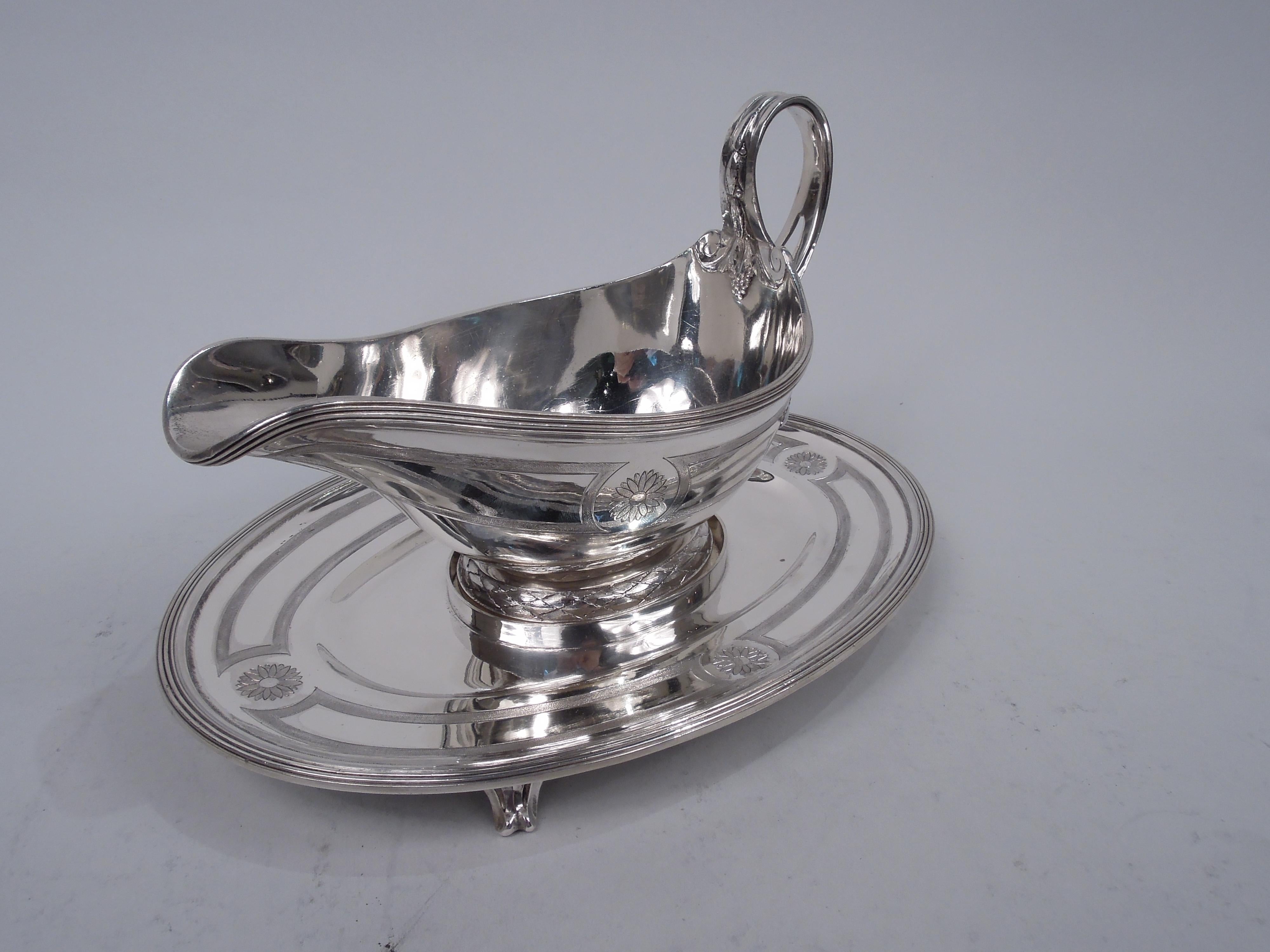 French Belle Epoque Classical 950 silver gravy boat on stand, ca 1910. Boat has ovoid bowl with helmet mouth and raised oval foot with imbricated leaf rim. High-looping and split leaf-mounted handle with armorial engraved in beaded oval frame. Stand