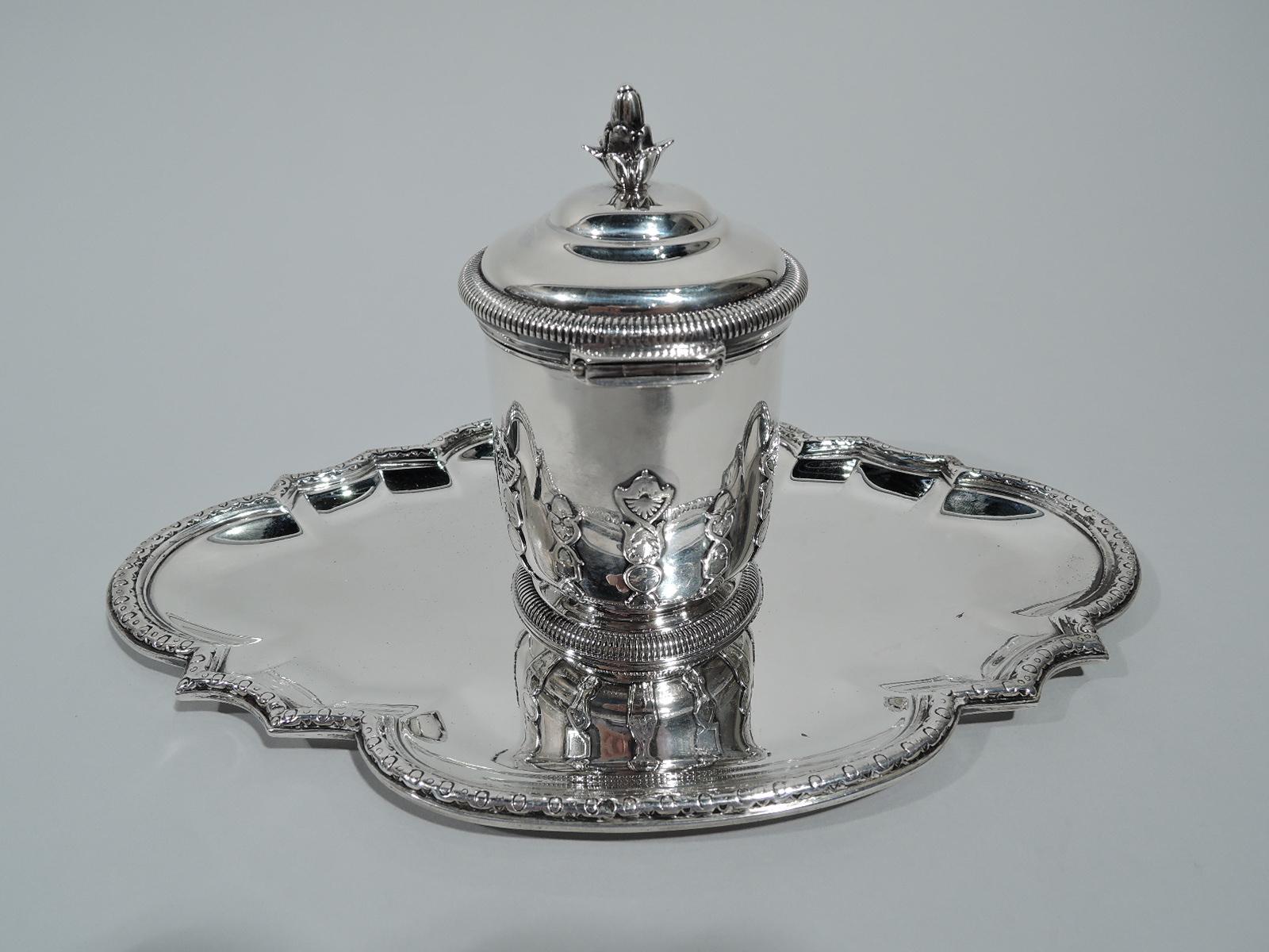 French 950 silver inkwell on stand, circa 1910. Straight sides with vertically applied strapwork bands; curved bottom and raised foot. Cover hinged and domed with flower-head finial. Gadrooned rims. Interior has engraved curvilinear border and