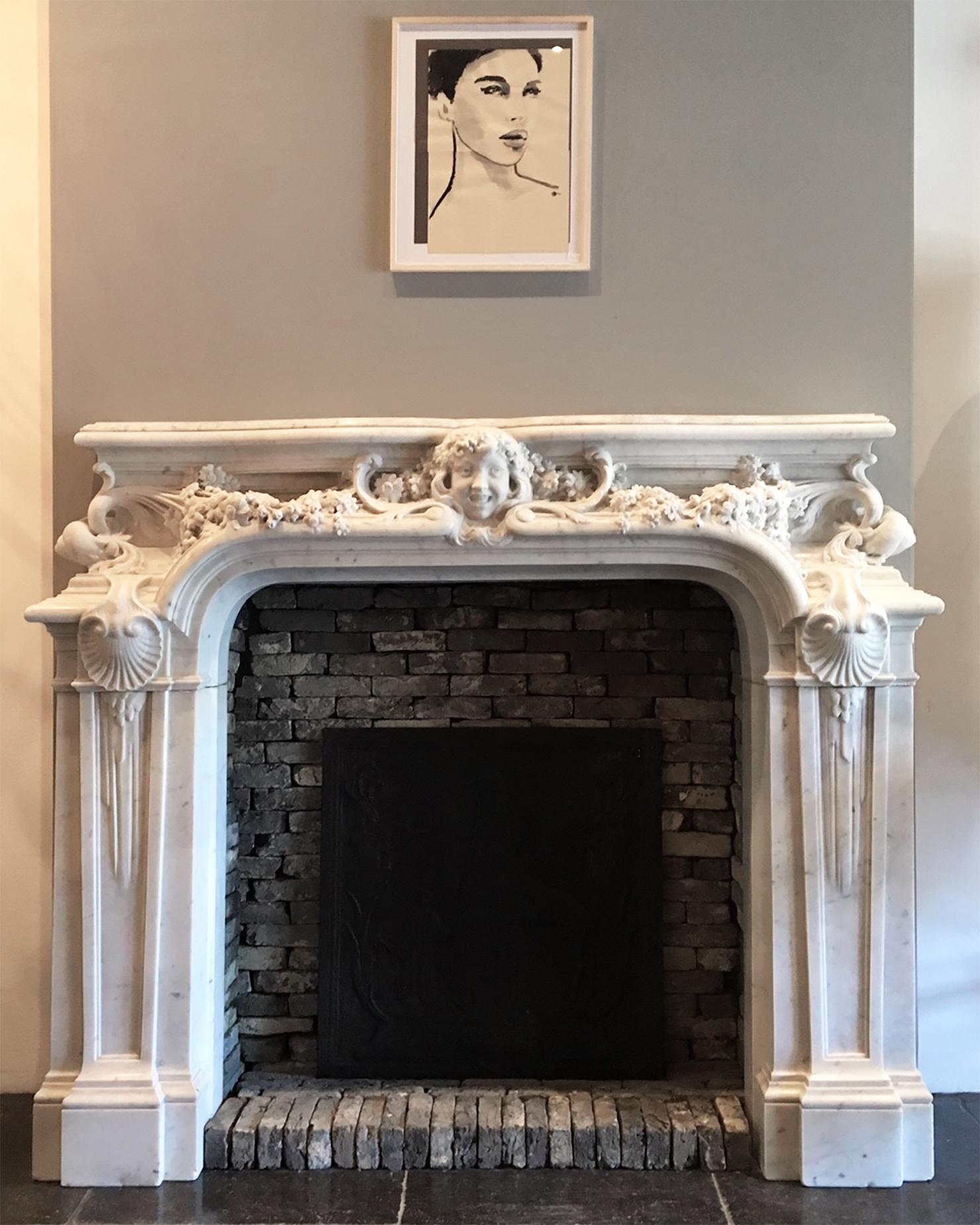 Large antique French mantelpiece of white Carrara marble, statuary quality. From the Belle Époque period in Classical Art Nouveau style. The central cartouche has the portrait of a grinning girl, flanked to either side by finely carved guirlandes of