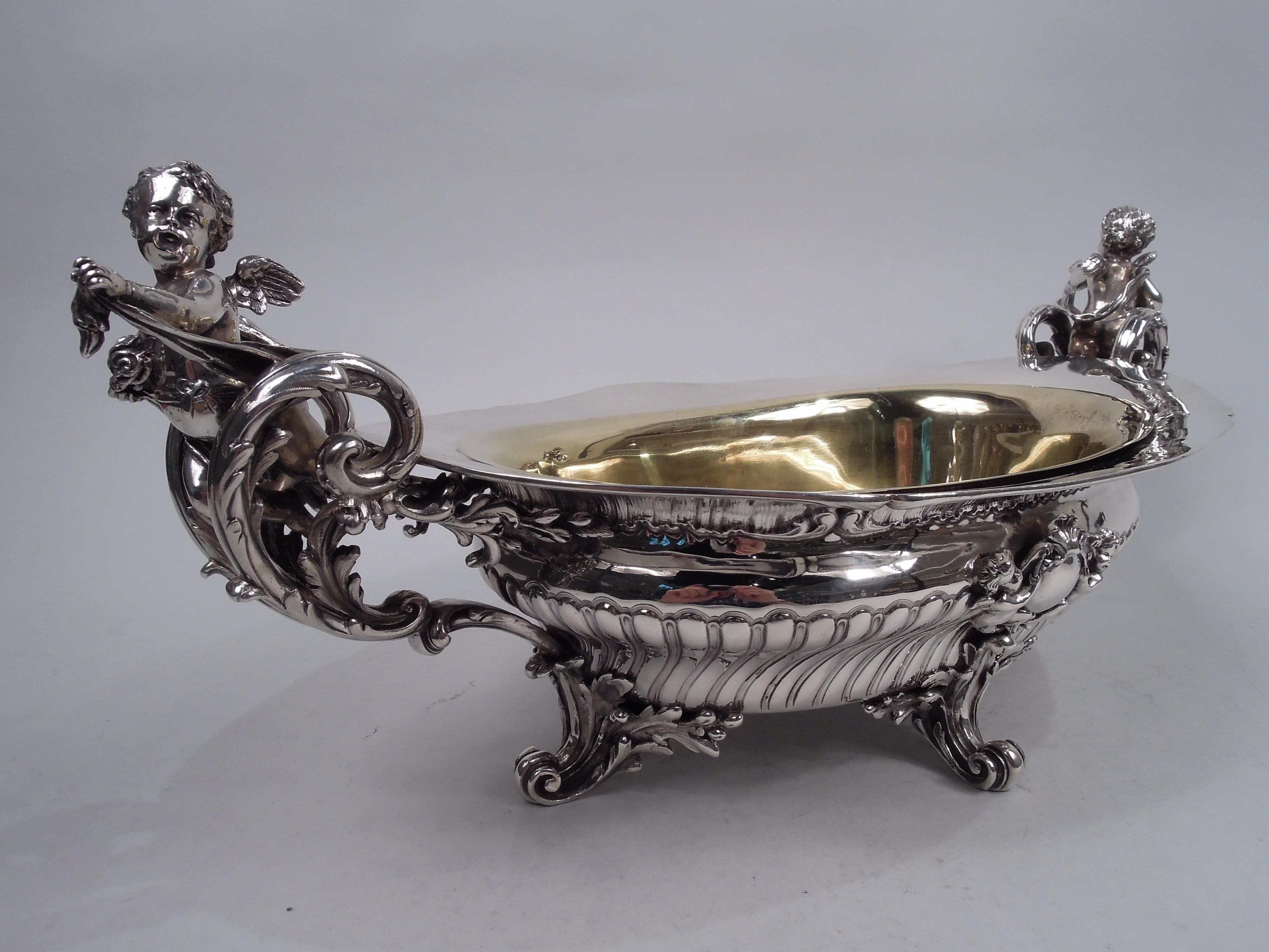 Belle Epoque Rococo 950 silver jardiniere centerpiece, ca 1900. Bombe oval bowl with wide and tapering rim. Embossed twisted fluting and applied round frames (vacant) with scallop shell crown supported by winged cherubs. Elaborate end handles: Cast