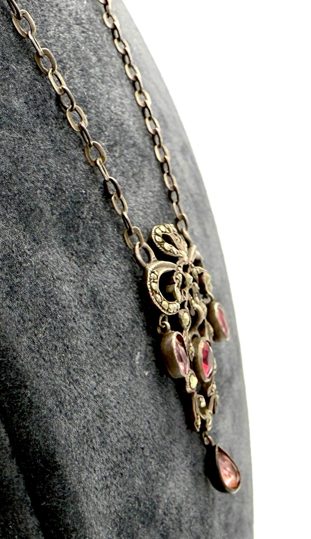 This Belle Époque necklace was created out of silver in France towards the end of the 19th century. The design of the pendant shows a smaller and a larger bow crowning a garland. The pendant is set with marcasites of varying sizes.
Three light pink