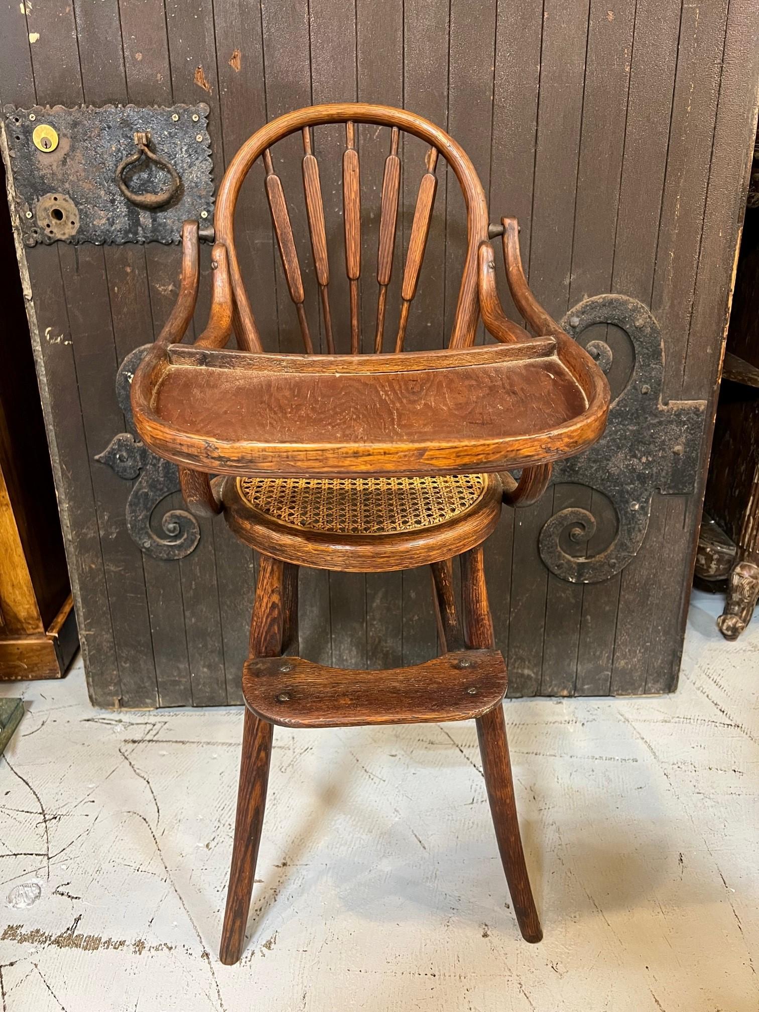 Beautiful antique French baby high chair crafted of bentwood with a round cane seat attributed to Michael Thonet. The child's high chair stands on four curved legs with a footrest on the front legs. The feeding tray table lifts up with a lock