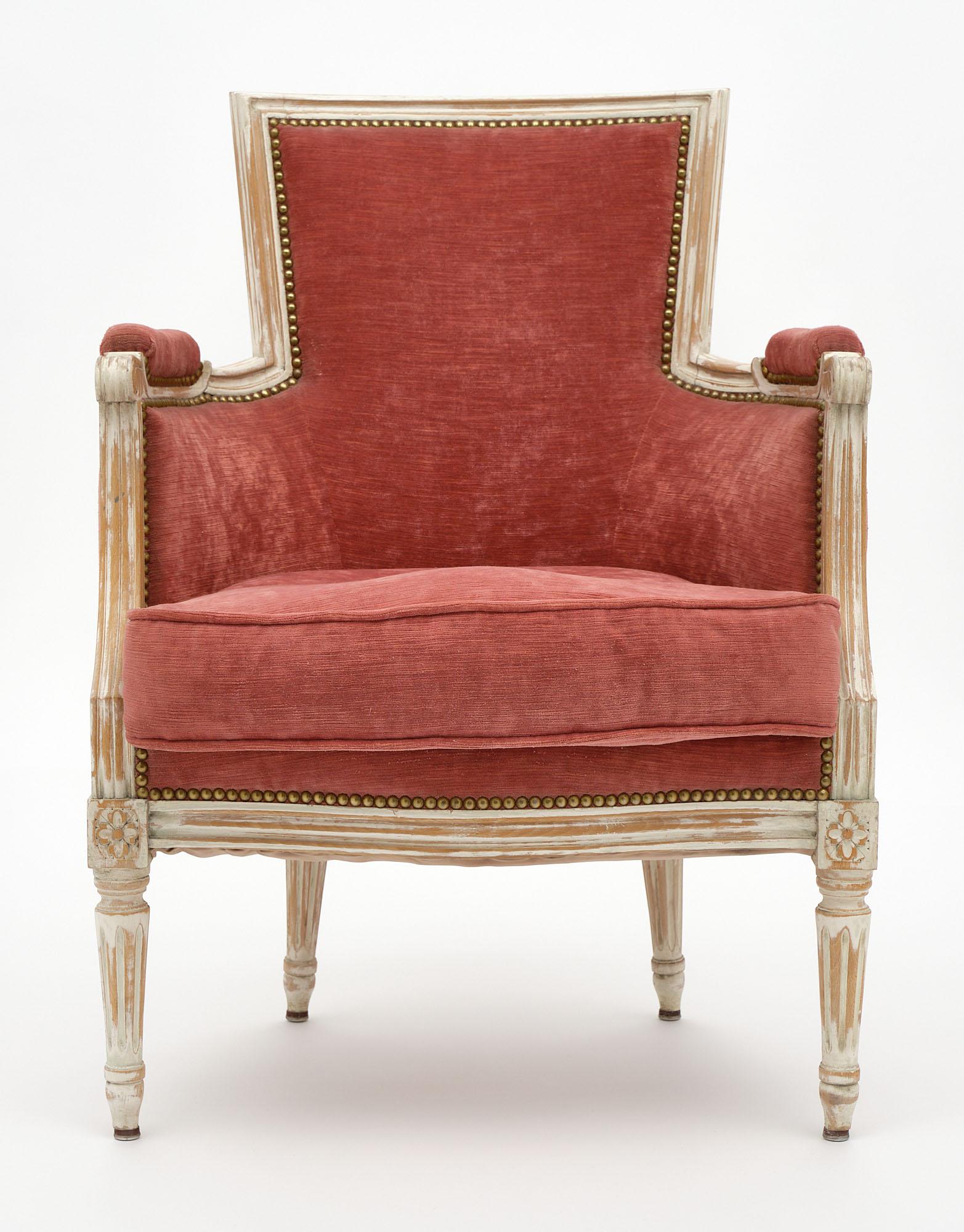 French bergère made of solid hand-carved beech wood with a beautiful patinated ivory colored lacquer. Original cotton velvet upholstery in a pink hue with the original brass tacks. Comfortable and in very good condition.