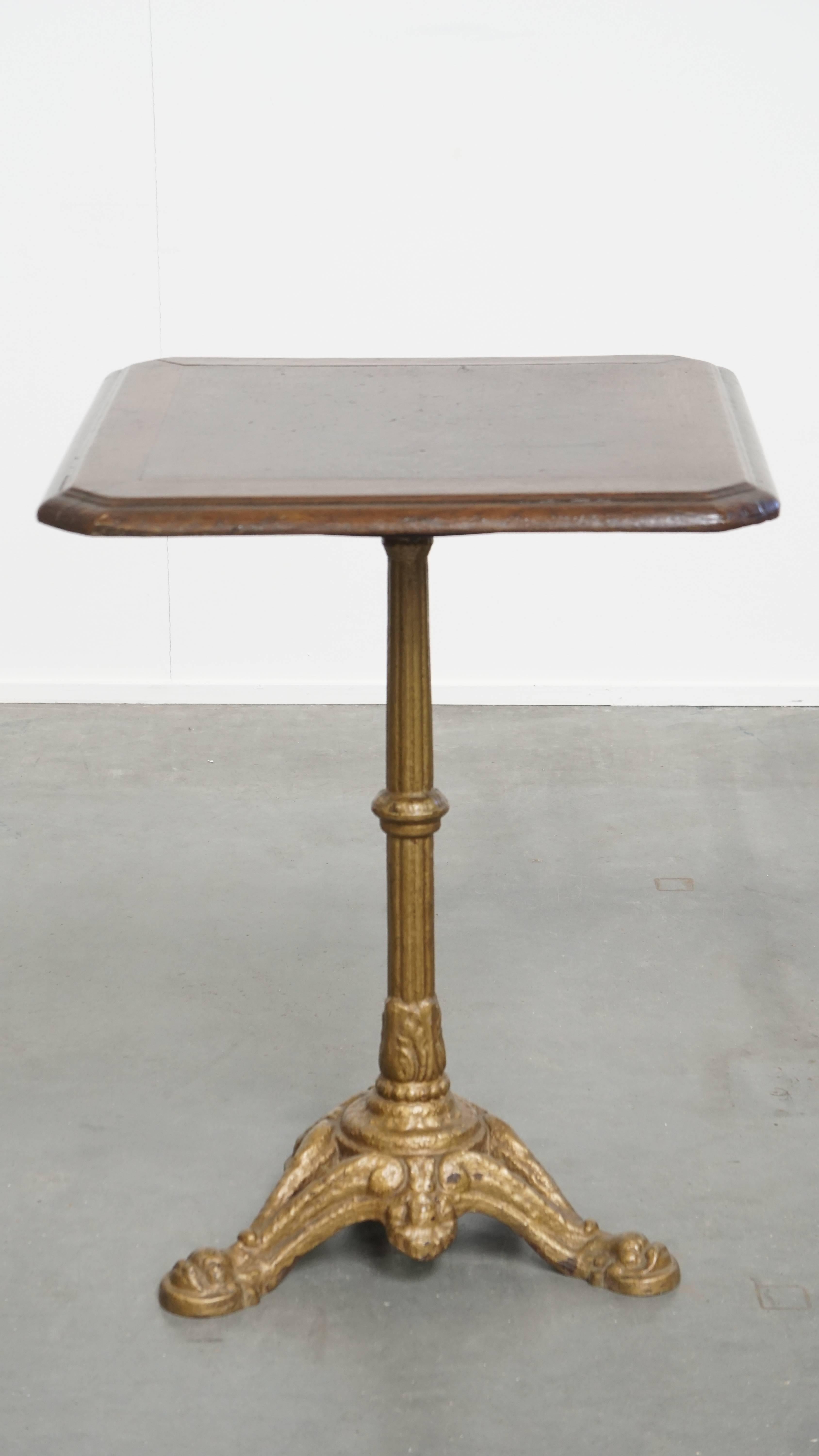 Offered is this stylish antique French bistro table featuring an elegant gold-colored cast iron base and a dark oak tabletop. 

This antique bistro table exudes charm and is a unique piece that brings character and elegance to almost any interior.