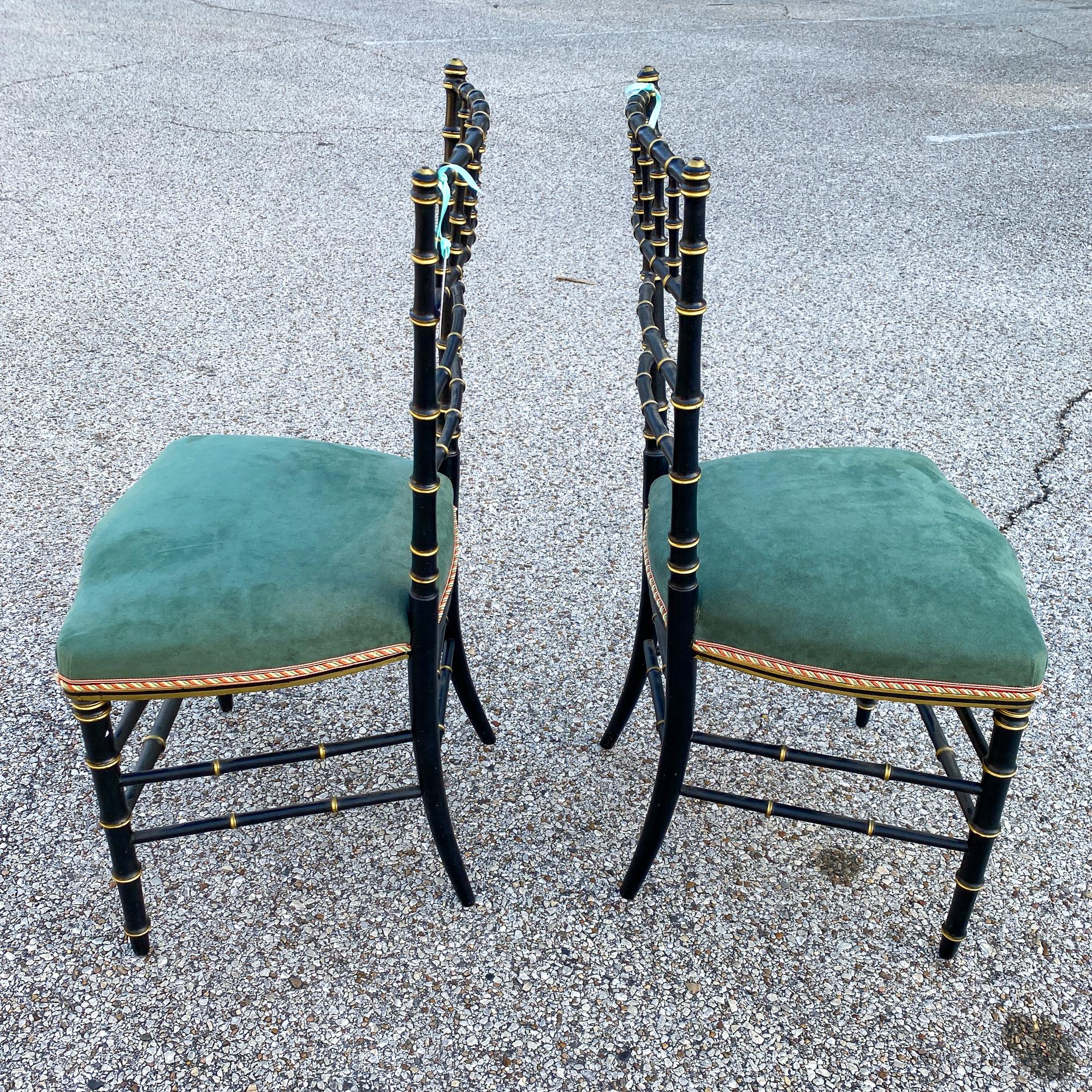 Each of these antique French Chinoiserie style chairs has a painted and waxed black finish with gilt accents and green suede upholstered seats. The rope trim around the seat edge is red, green and gold. The chairs have a faux bamboo look in their