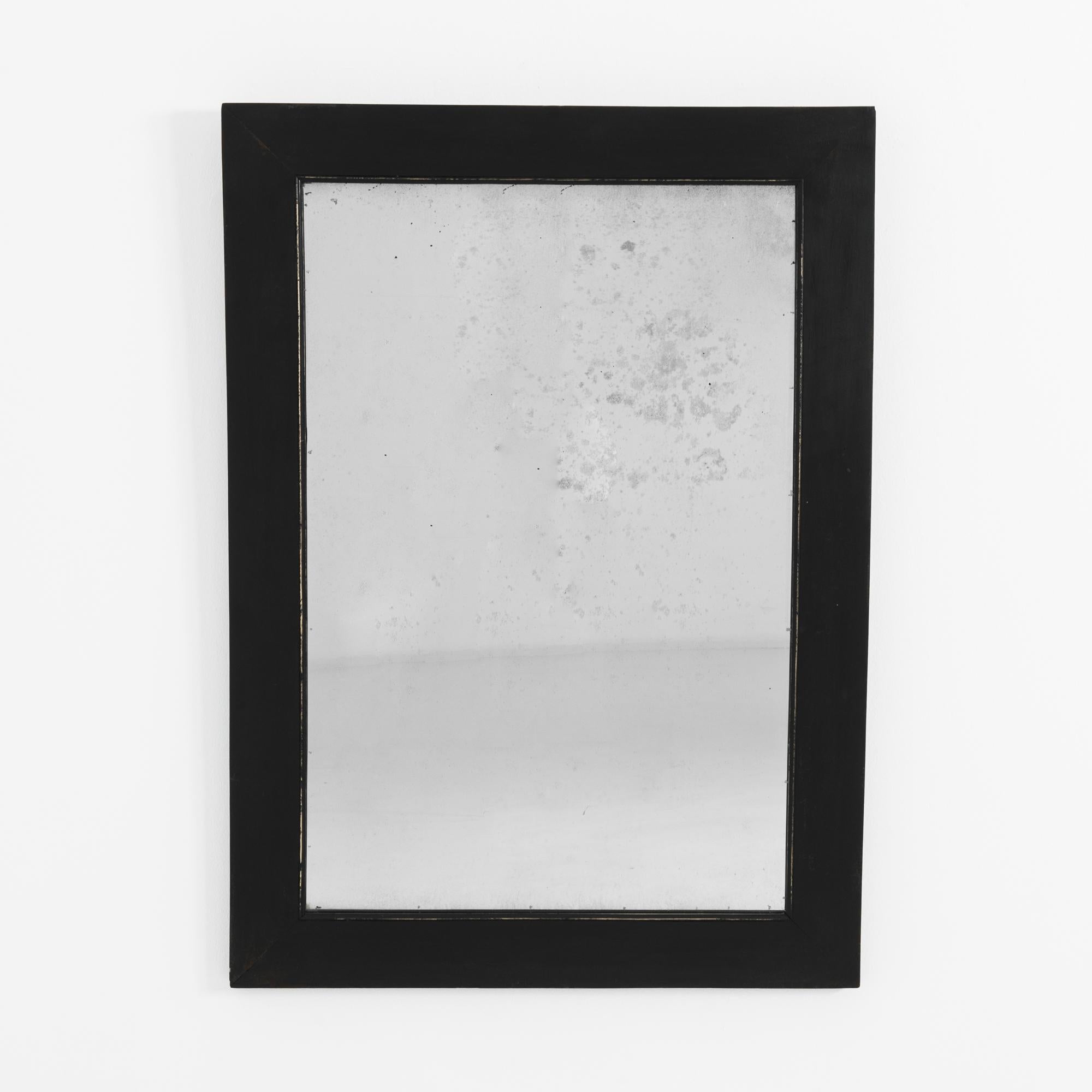 A wooden mirror from France, circa 1900. Elegantly framed in black, a subtle inset profile elevates this simple mirror with the detailed eyes of period craftsmen. The subtle patina of the mirror surface enhances your reflection with a note of