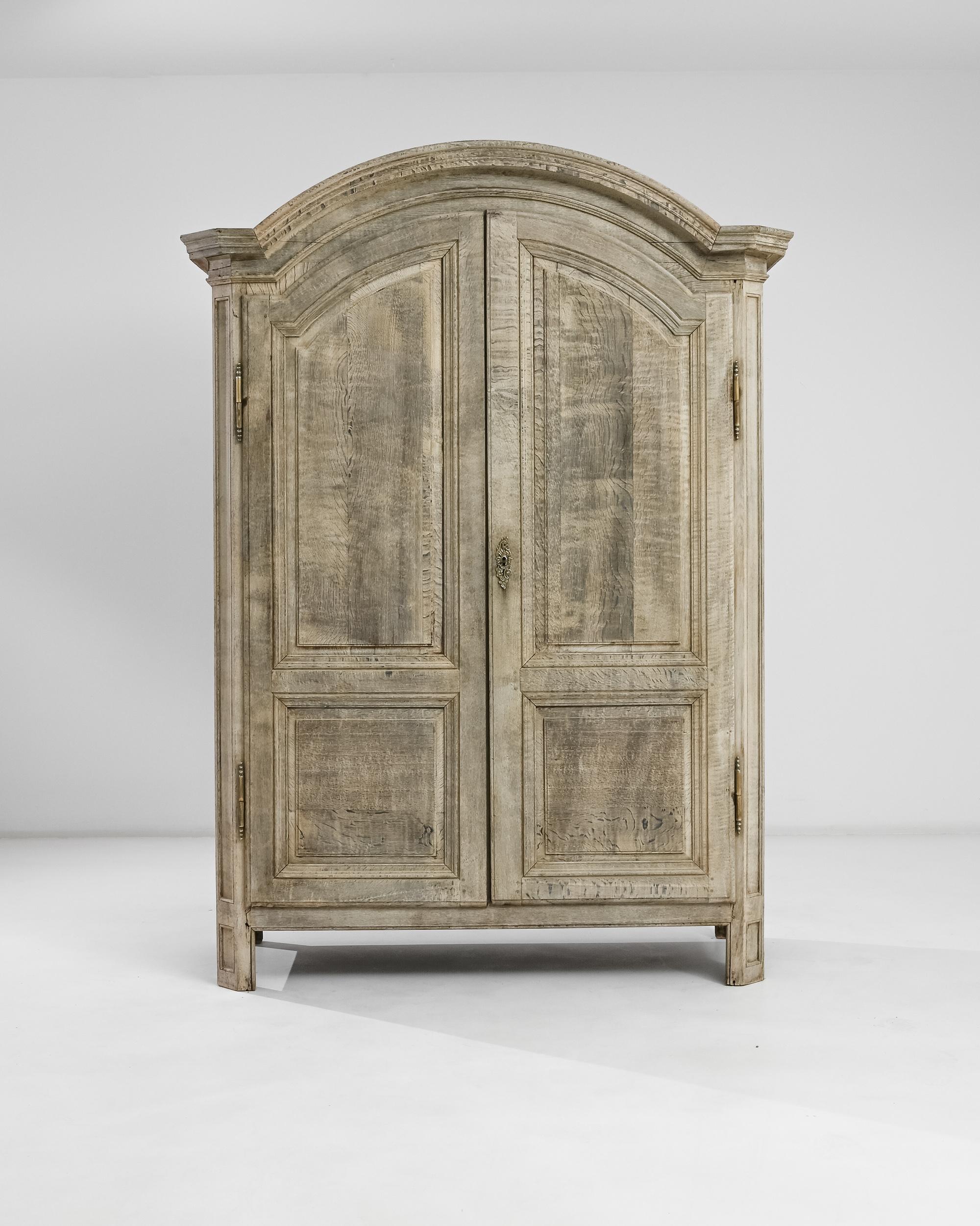 This bleached oak double-door armoire was produced in France, circa 1850. An antique gem with a curved cornice top, elevating above seven feet and garnished with gilded hardware. The ample three-shelves interior showcases the original russet tone of