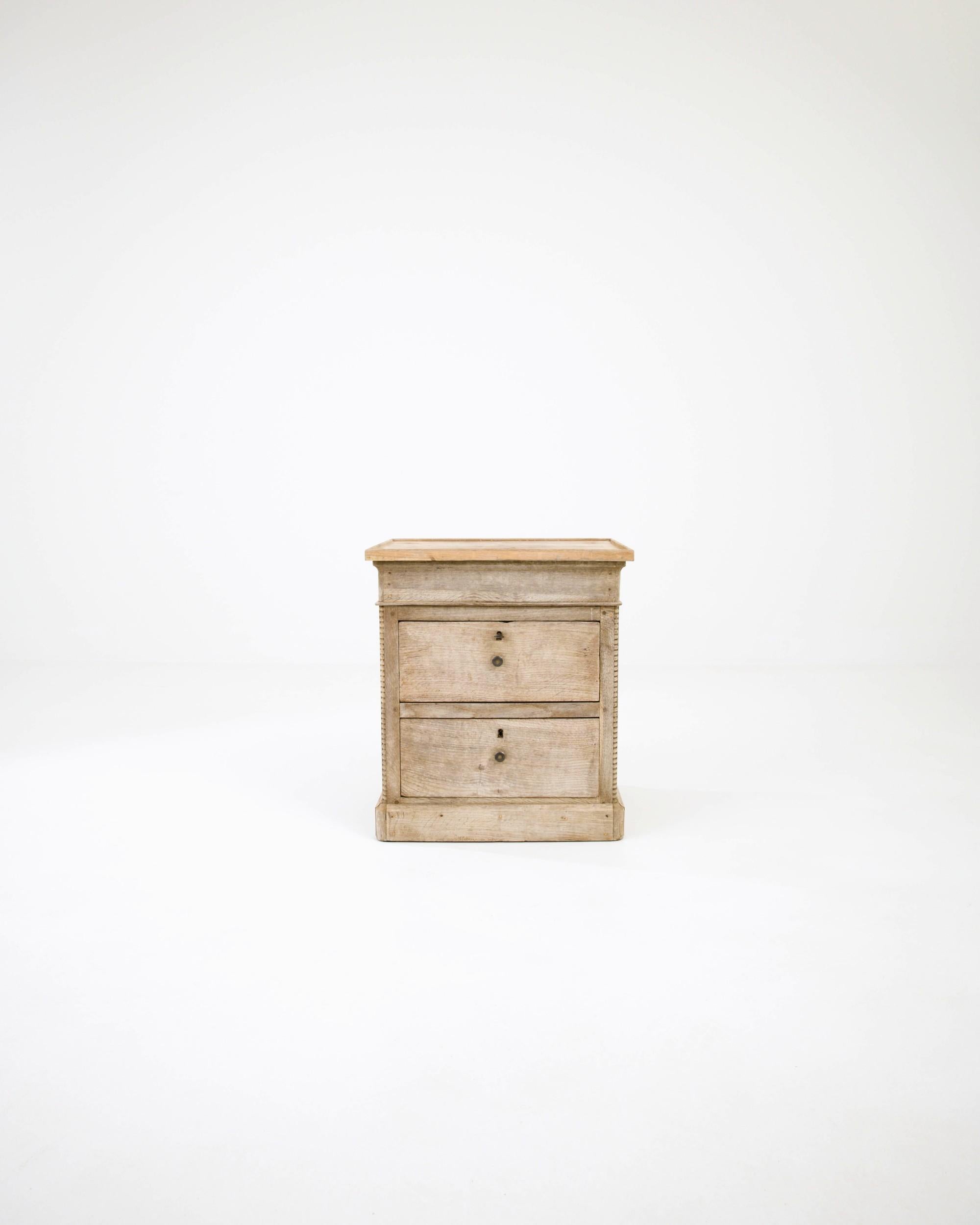 This 19th-century oak night stand originates from France. It features two deep drawers with original brass knobs, and it is adorned with carved beads along the sides. The plinth base and profiled top, gives the chest a resemblance to an ancient