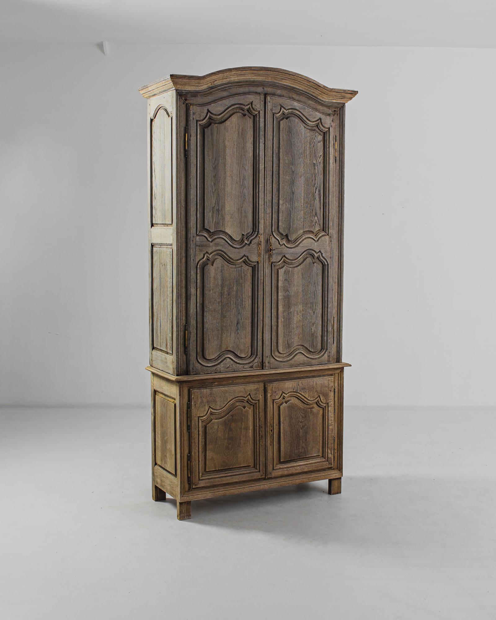 This antique bleached oak cabinet was made in France. The precision of the carved contoured paneling and its smooth finish convey a refined air suffused with rustic warmth. Slightly elevated, it features four shelves in the compartment above and two