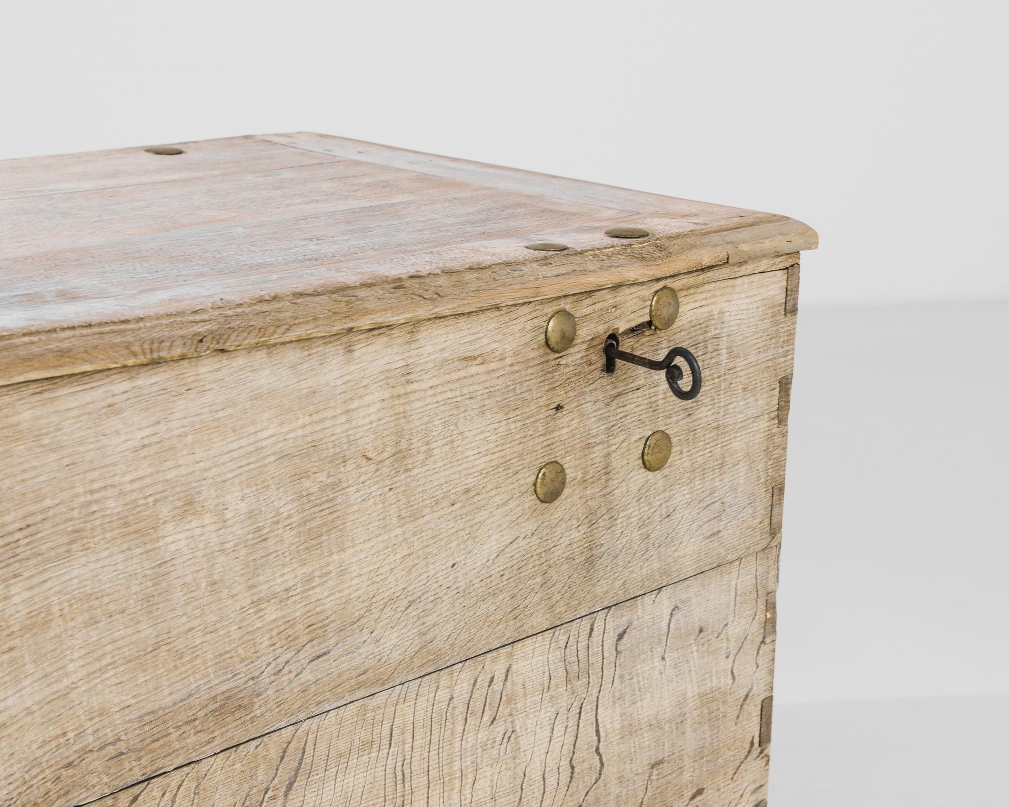 An oak trunk, made in France circa 1800. Dovetail joints give an appealing variation to the corners of the case: a decorative accent born of skillful craftsmanship. Large brass studs frame the key holes, which lock with an original spiral key. The
